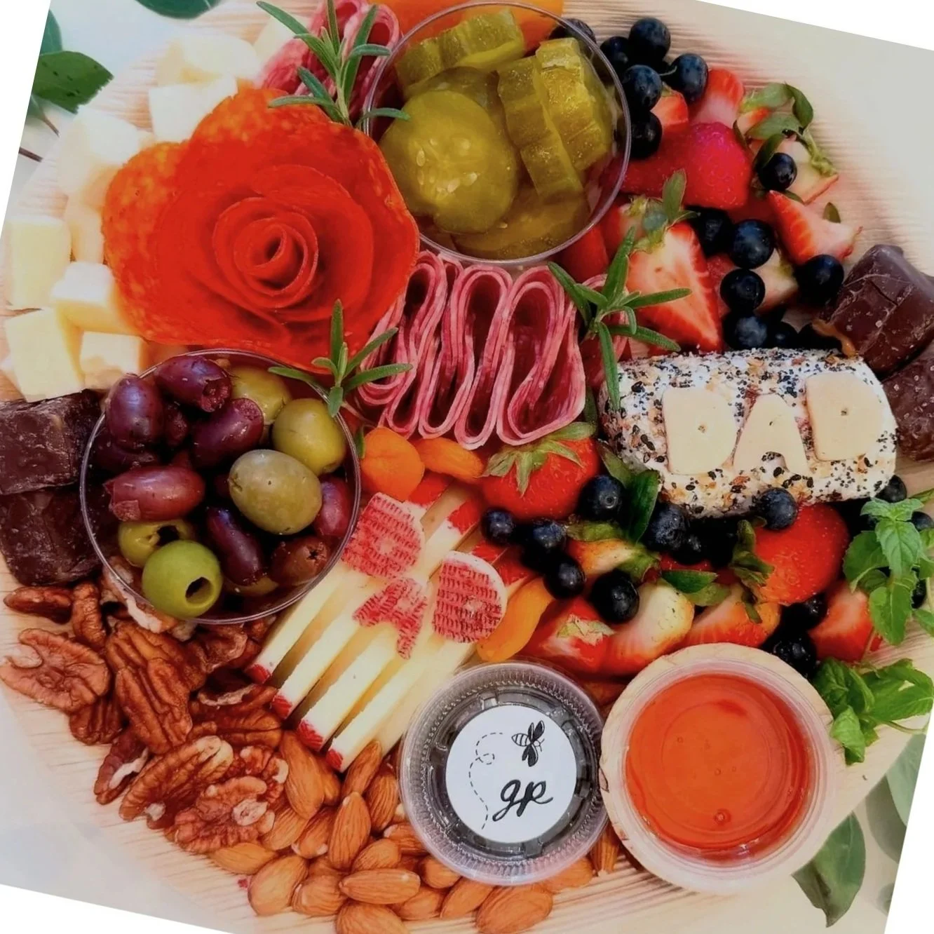 A charcuterie board with cheese, grapes, almonds, strawberries, blueberries, pickles, cured meats, crackers, and honey.