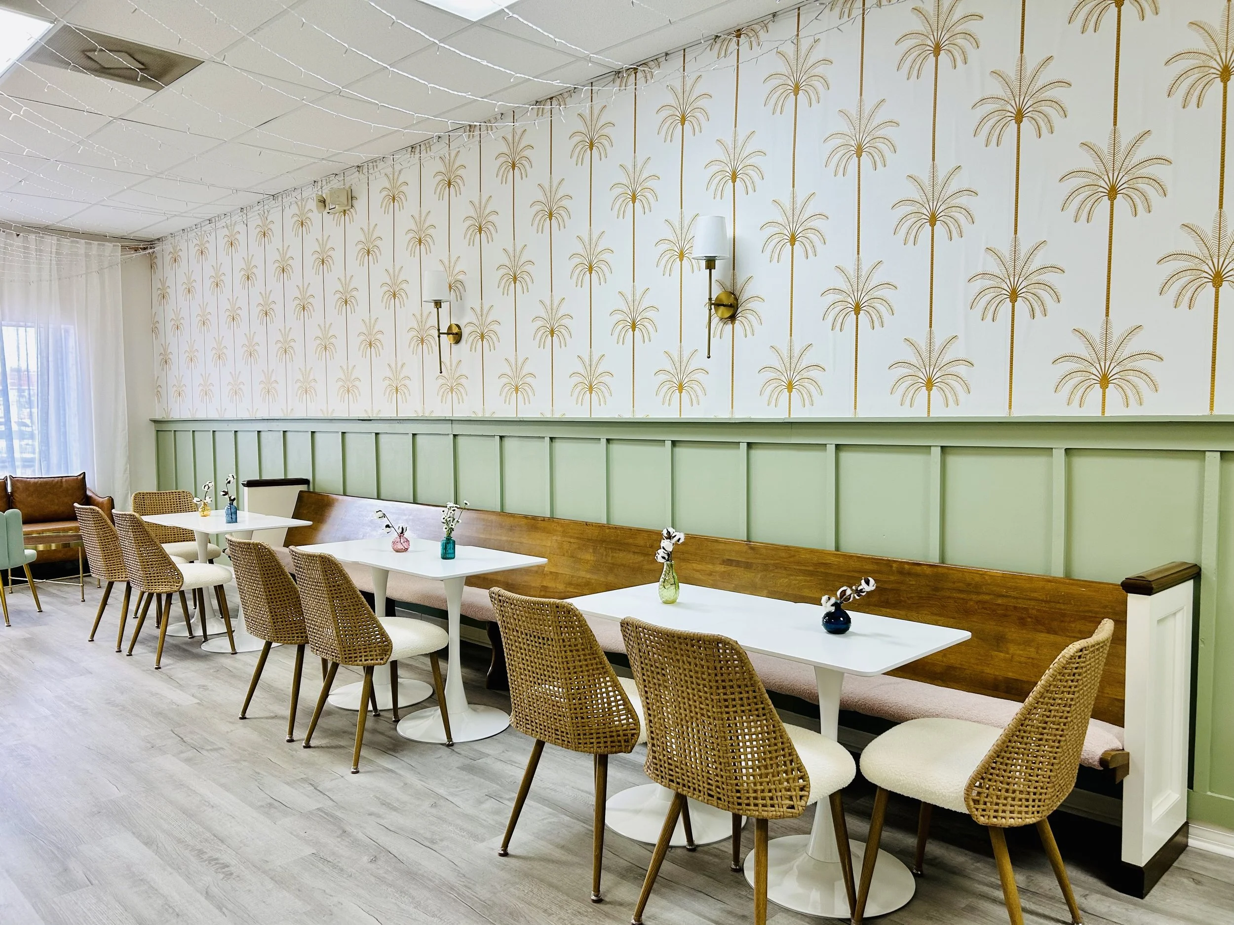 seating area with church pew with dusty rose pink seat, refinished wood, comfy cream chairs, colored vases with small flowers, mint board and batten wall with tropical wall paper, cream with gold palm trees.