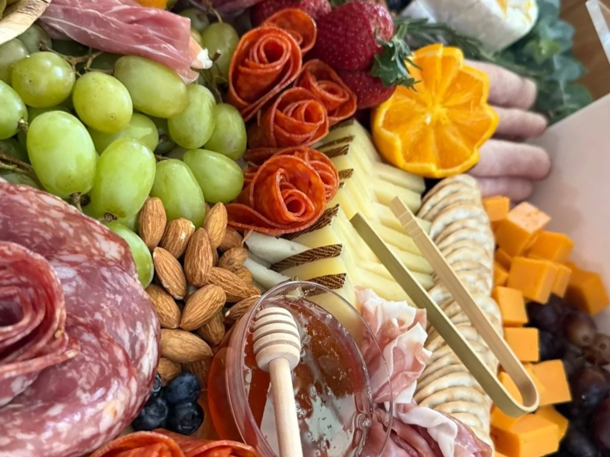 Cheese, grapes, almonds, strawberries, honey, sliced fruits, meats, and cheeses on a charcuterie board.