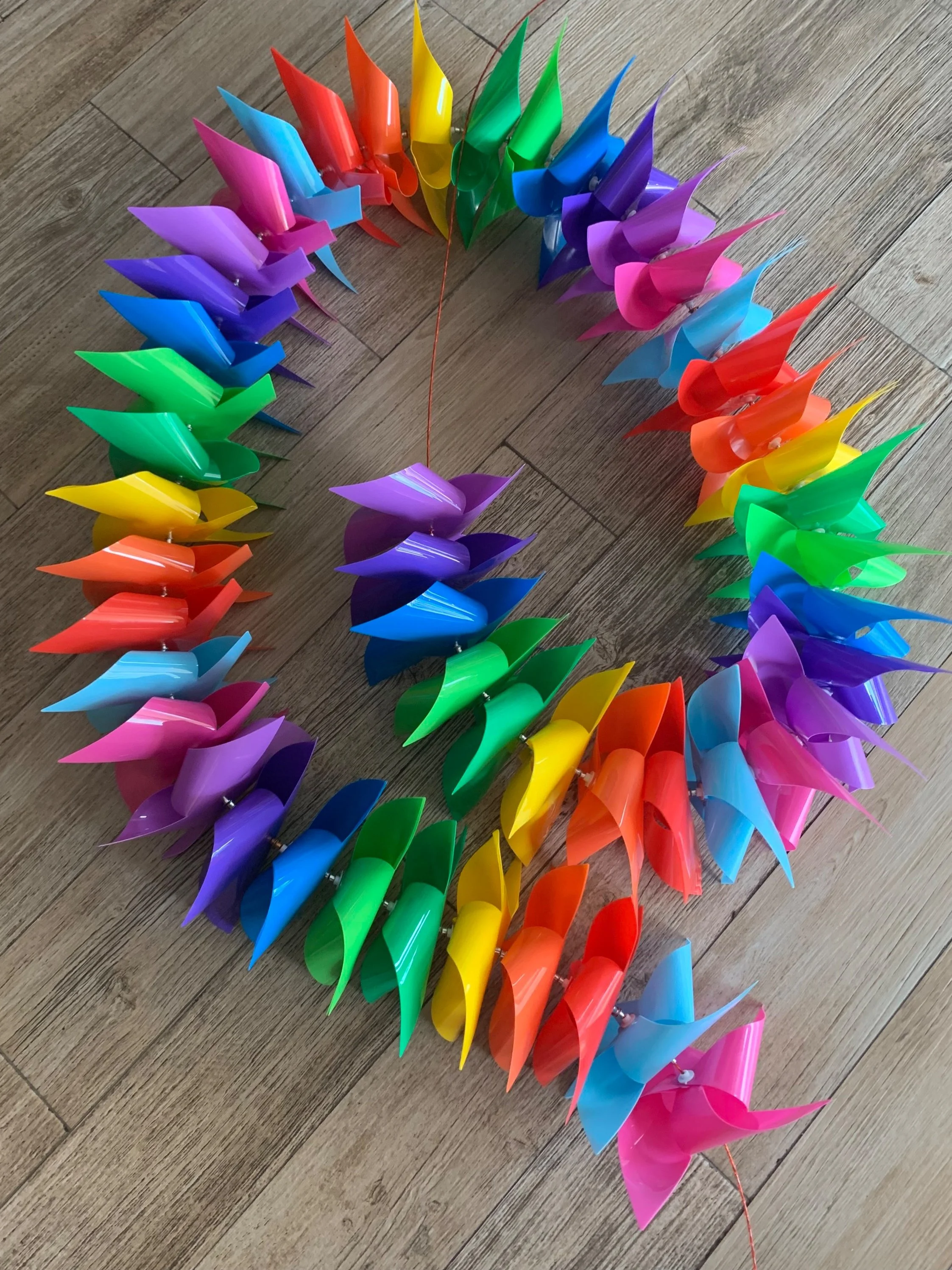 Colorful plastic pinwheels arranged in a circle on a wooden floor.