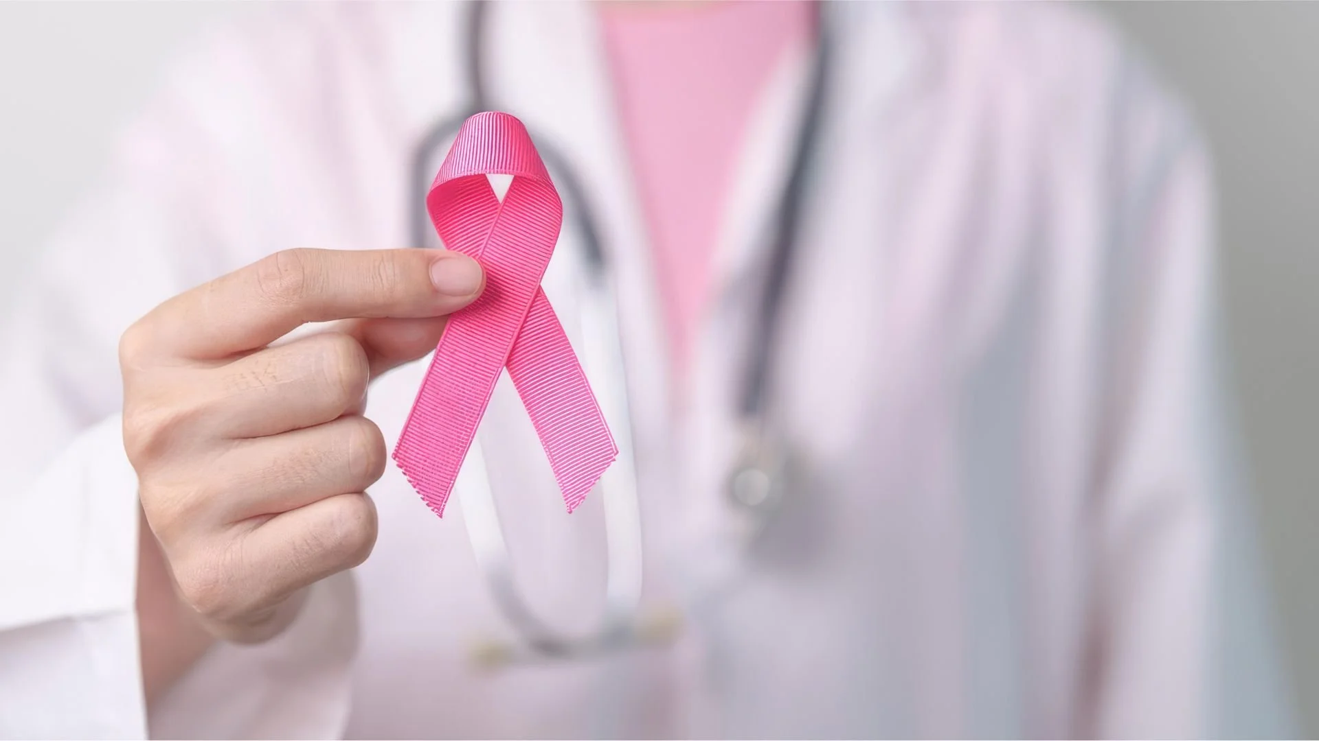 Doctora sosteniendo un listón rosa, recordatorio de la prevención del cáncer de mama y cervicouterino