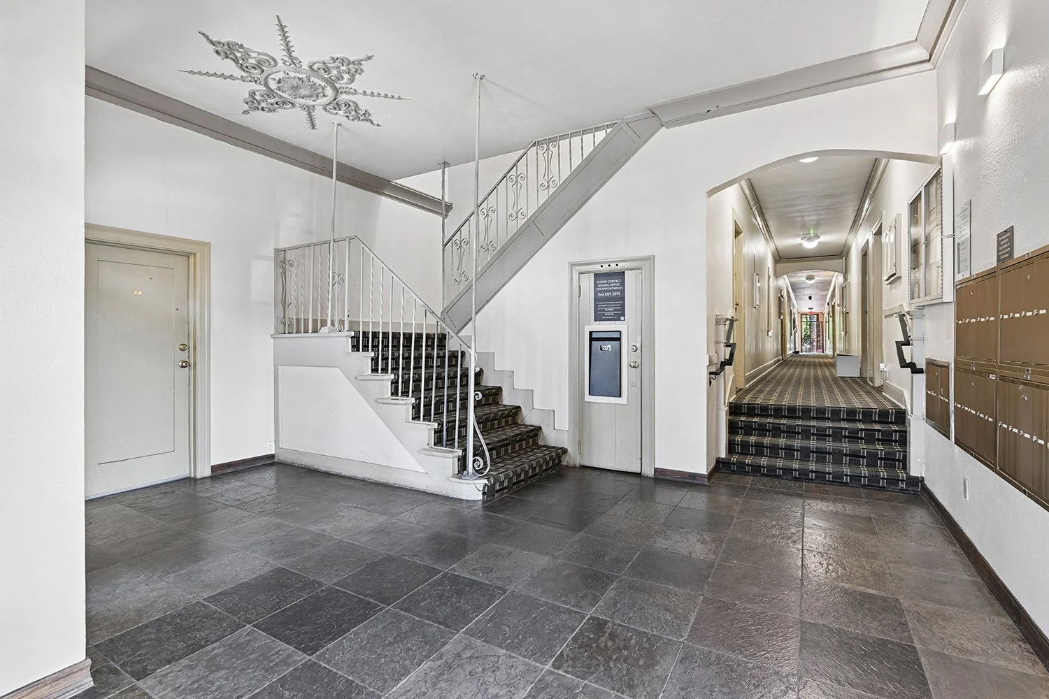 Lobby in Cahuenga apartments with unique architectural details, wood entry door, plants, and charming staircase. 