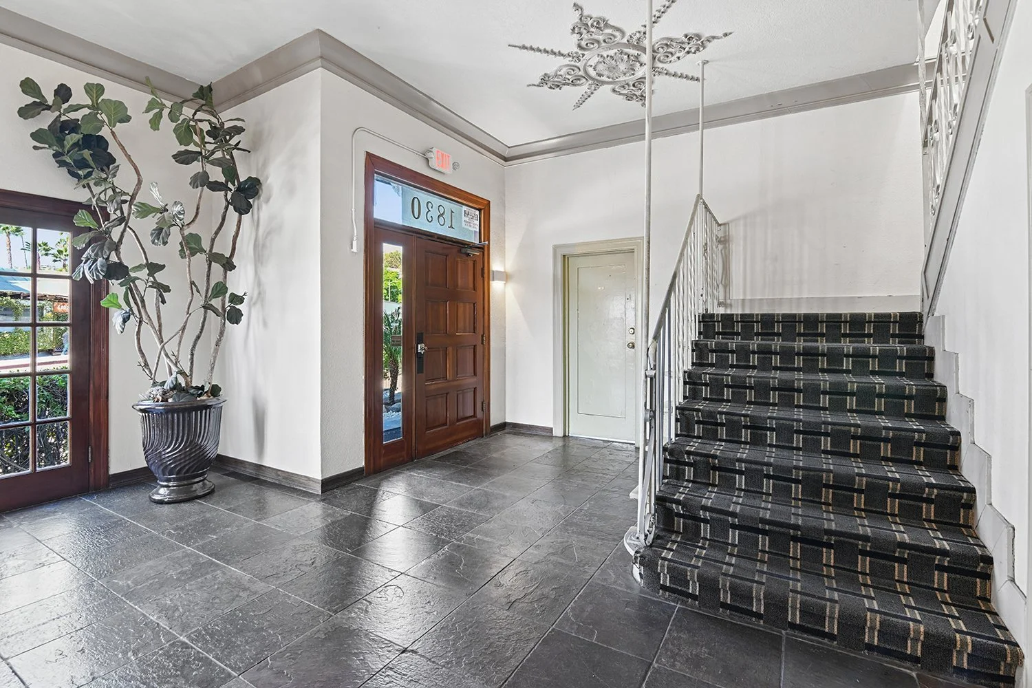 Lobby in Cahuenga apartments with unique architectural details, wood entry door, plants, and charming staircase. 