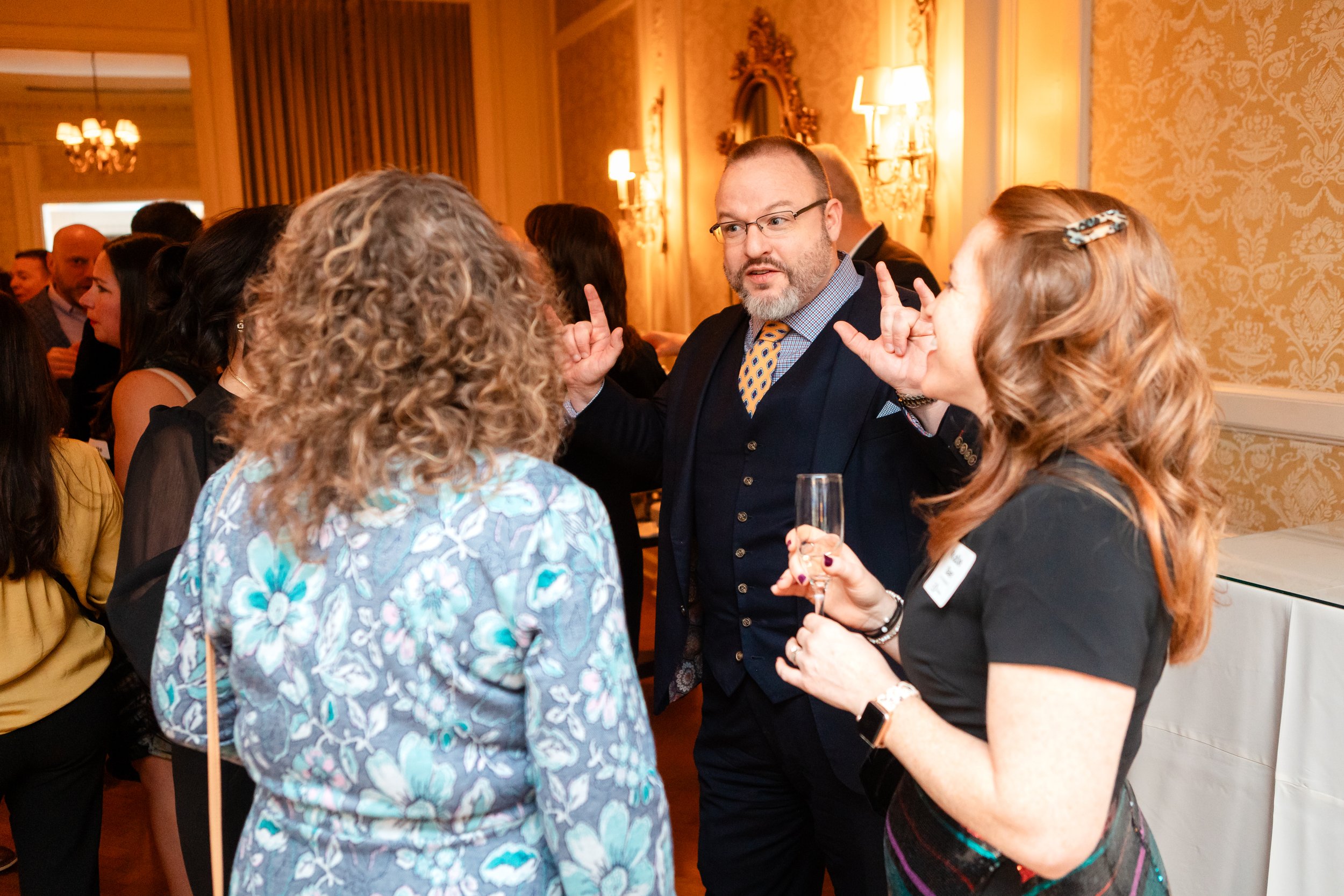 Gentry performing walk-around mentalism for two guests at a corporate cocktail reception in a chandeliered ballroom.