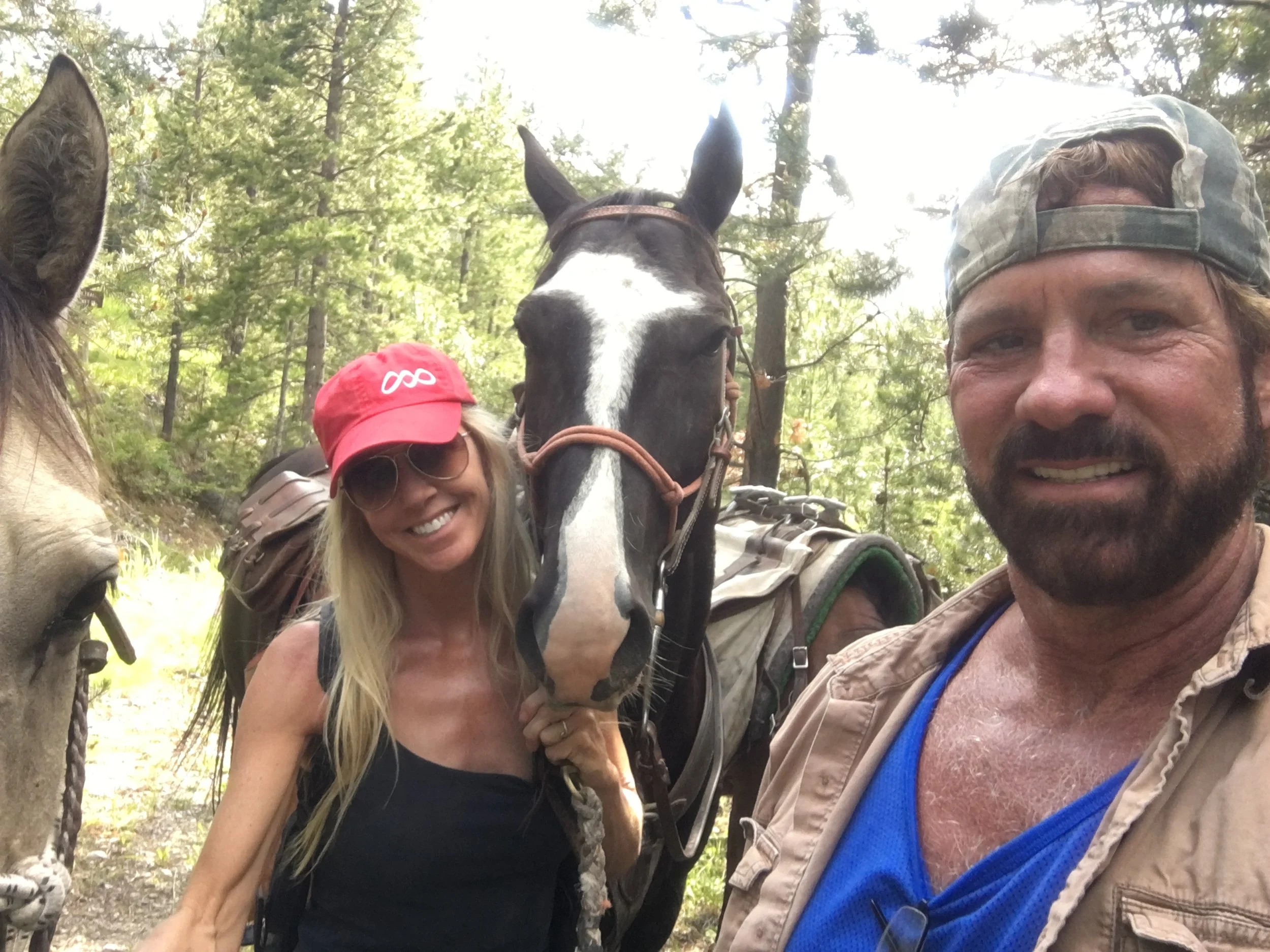 Man and woman smiling with two horses in a forest.
