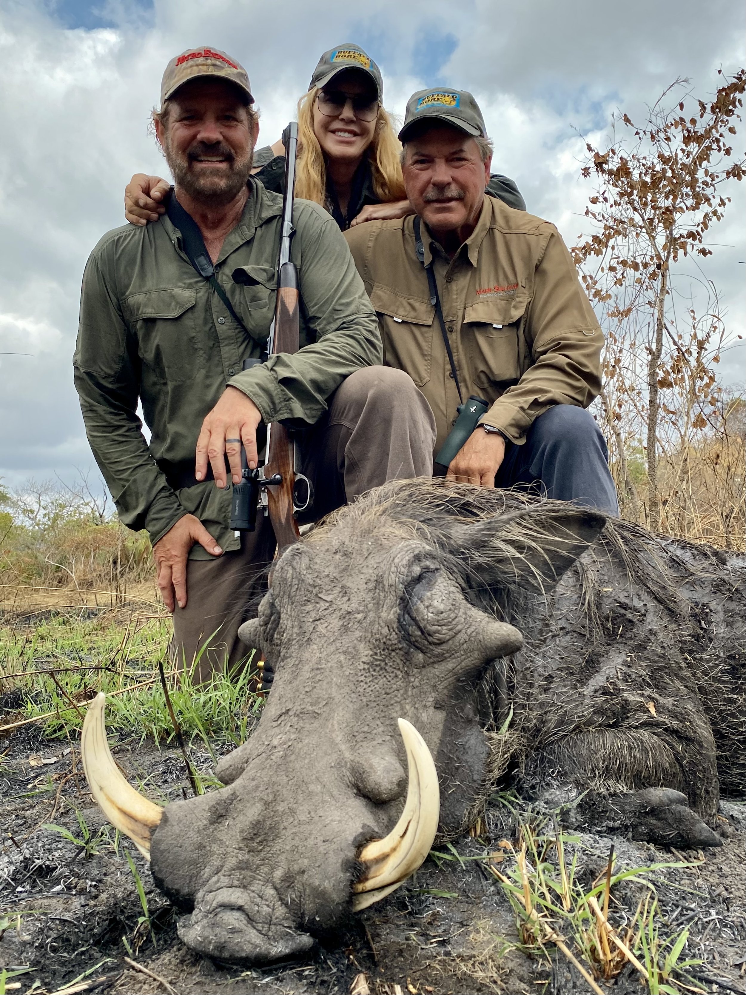 Three people in outdoor clothing posing with a hunted warthog.
