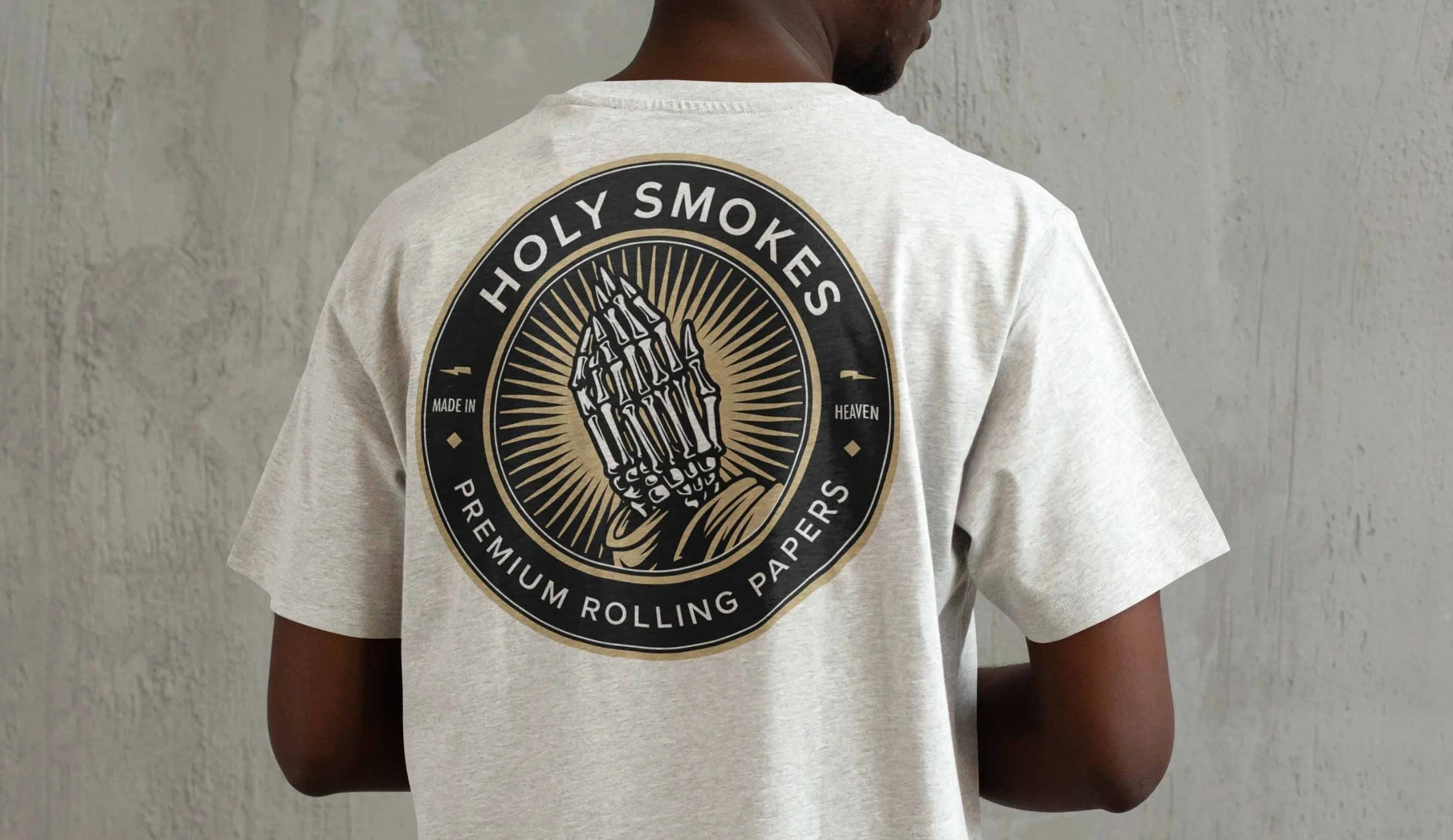 Person wearing a white t-shirt with a circular logo on the back featuring a skeletal hand holding a cigarette and the text "Holy Smokes" and other details.