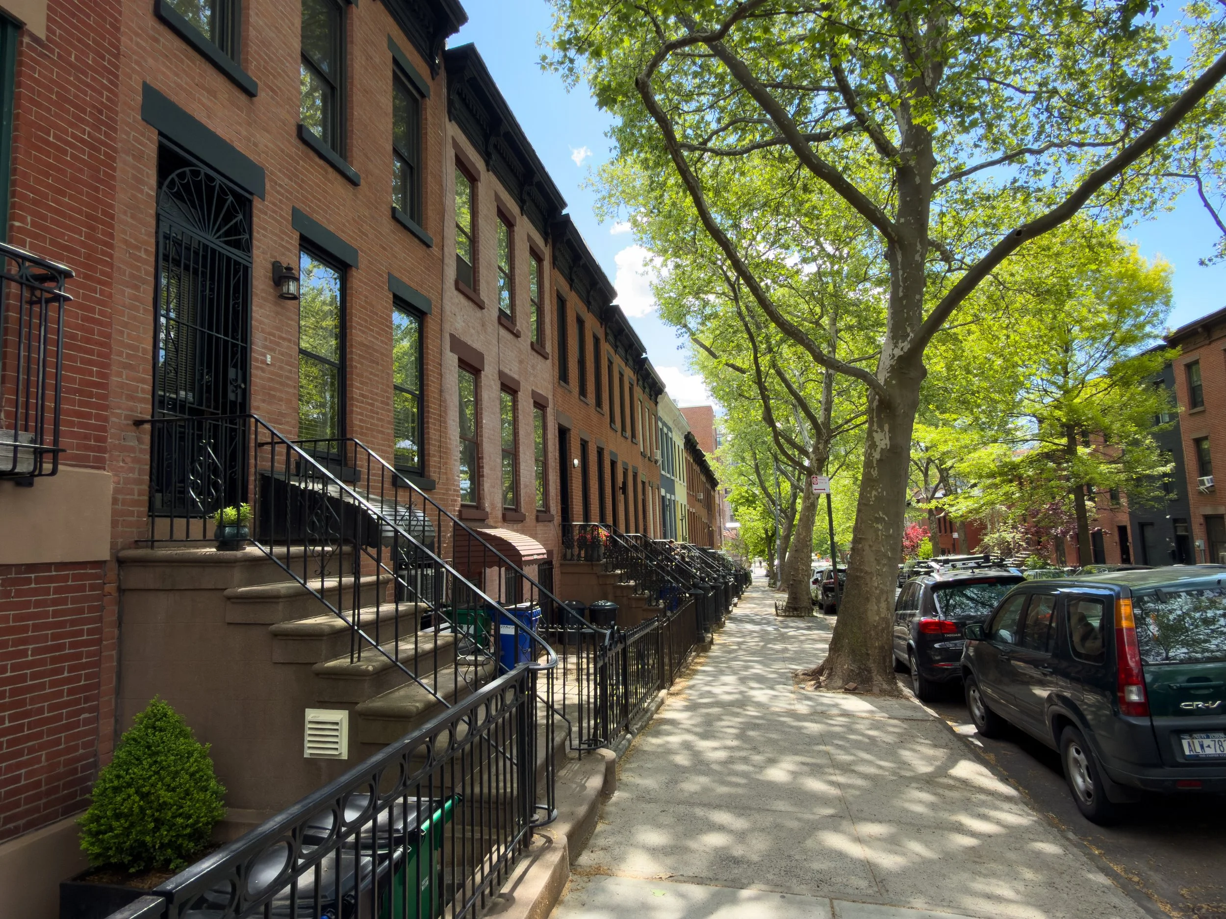 Tree-lined sidewalk beside brick townhouses in Gowanus, Brooklyn, NYC, reflecting the neighborhood’s residential streetscape and low-rise real estate character.