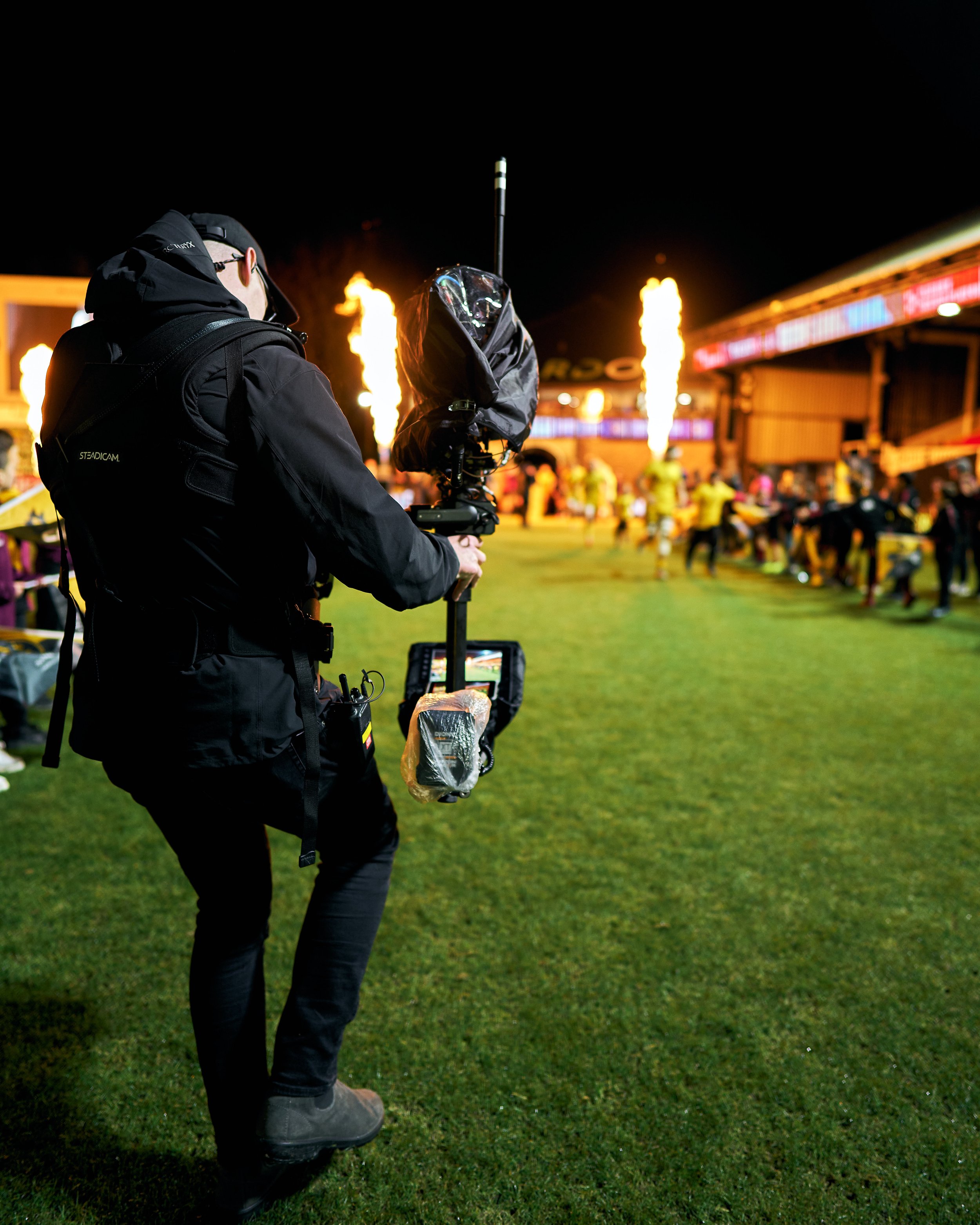Photographer filming at a night sports event with fire effects in the background.