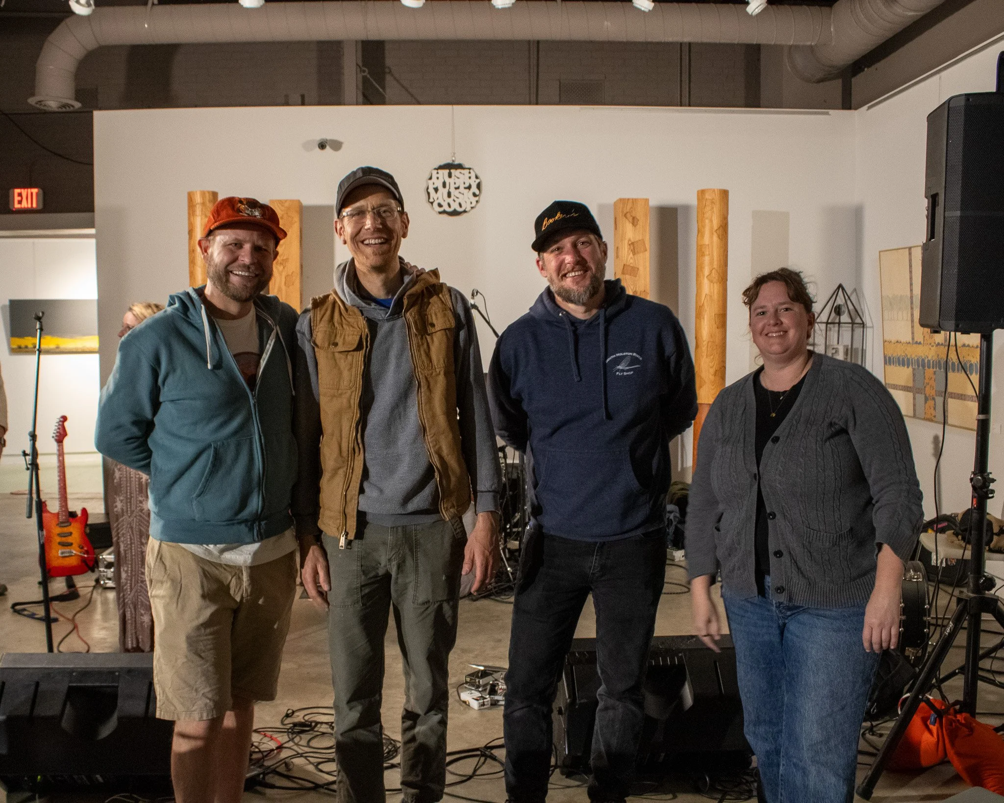 Group of four people smiling and posing in a music studio setting with instruments and sound equipment in the background.