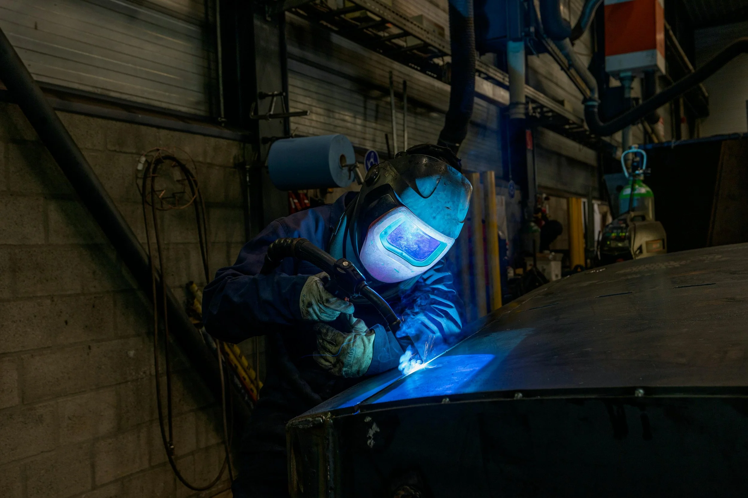 Professional welder performing TIG welding under dim lighting, with sparks and protective gear visible.