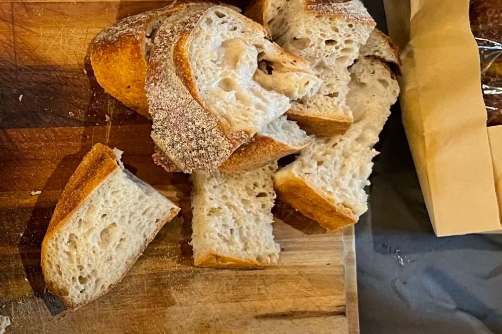Sliced rustic bread with a crusty exterior on a wooden cutting board.