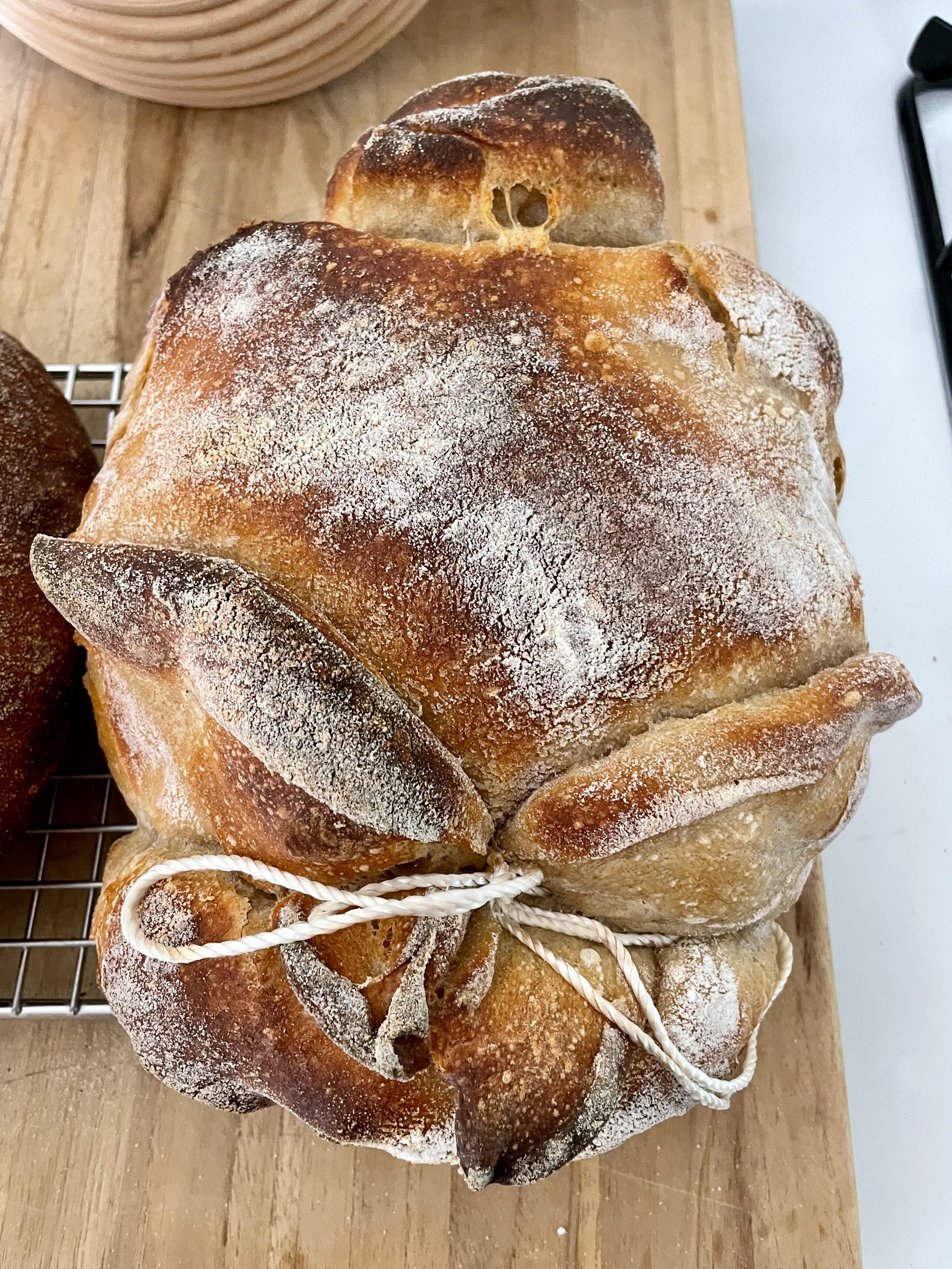 A rustic loaf of bread tied with white string, with a dusting of flour on top, resting on a wooden surface.