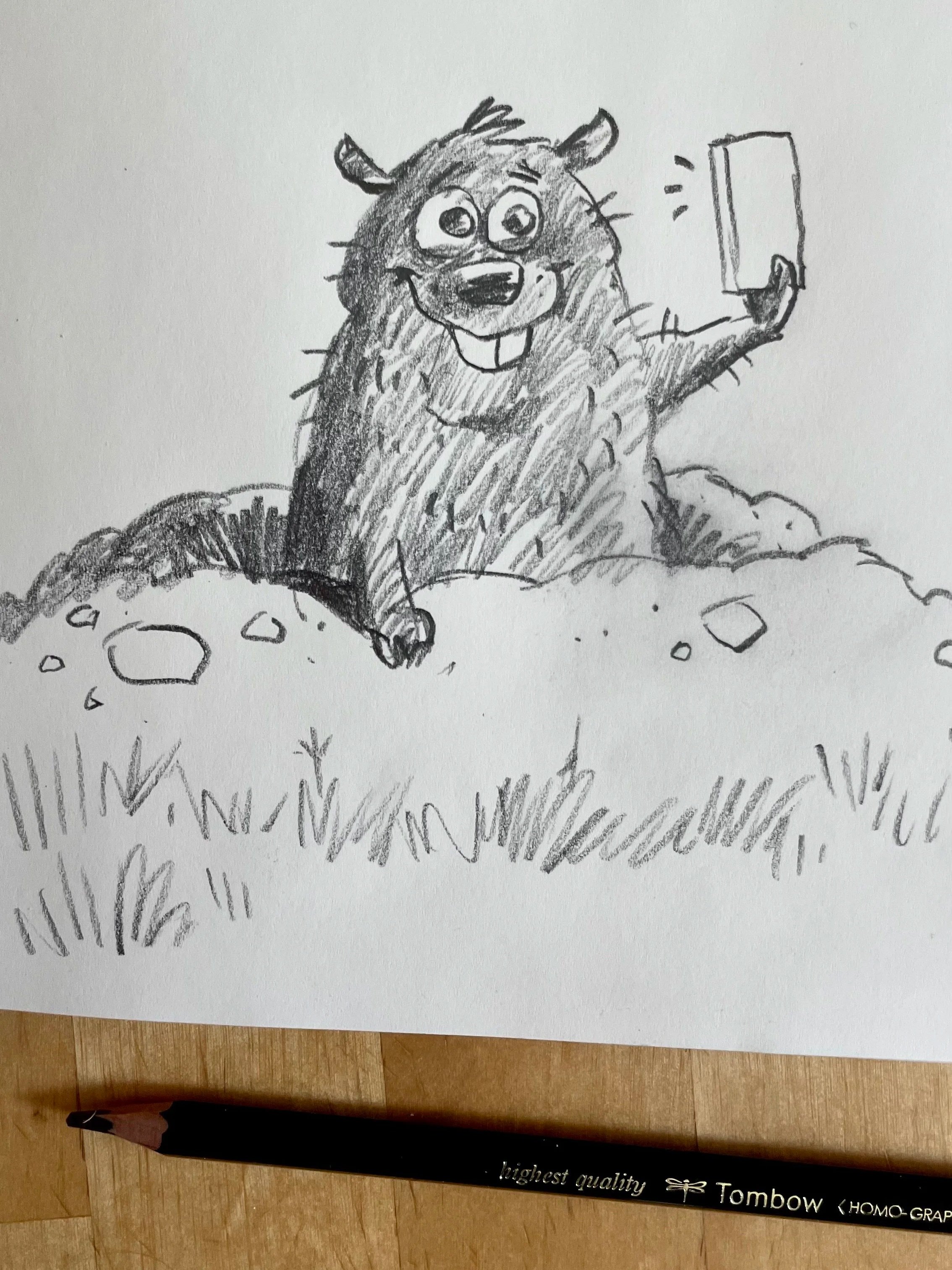 A hand-drawn sketch of a happy cartoonish dog taking a selfie with a smartphone. The dog has big eyes, a big smile showing teeth, and is sitting on some rocks or uneven ground. There is a close-up of a black-colored pen at the bottom of the image, which has some text on it, including the words "highest quality" and "Tombow".