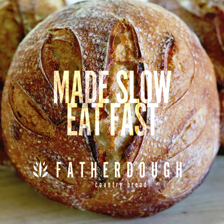 A round loaf of country bread with a decorative score on top, dusted with flour.