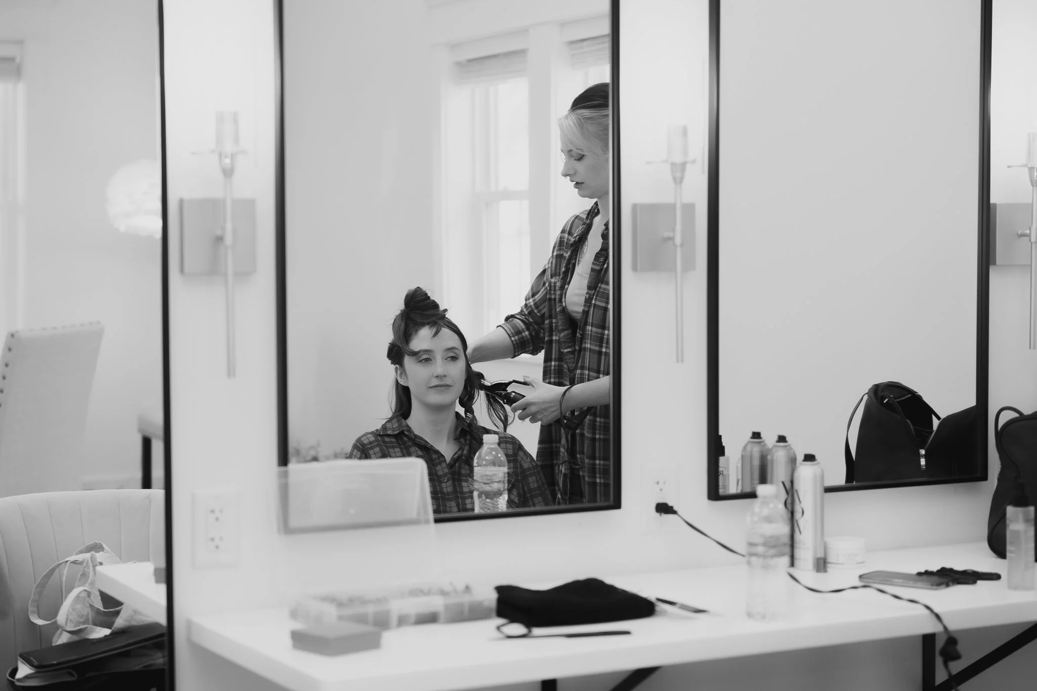 A hairstylist curling a woman's hair in a salon with mirrors and styling equipment.