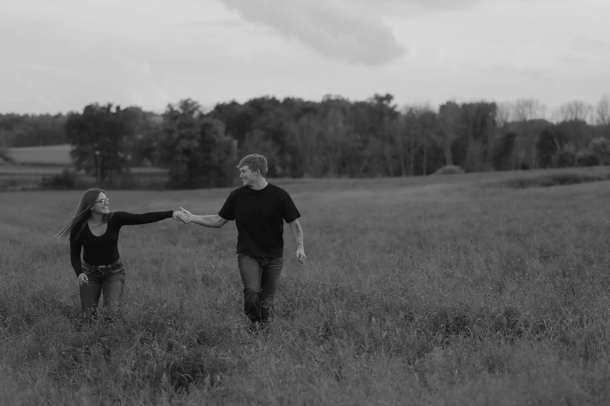couple smiling at each other holding hands in a field