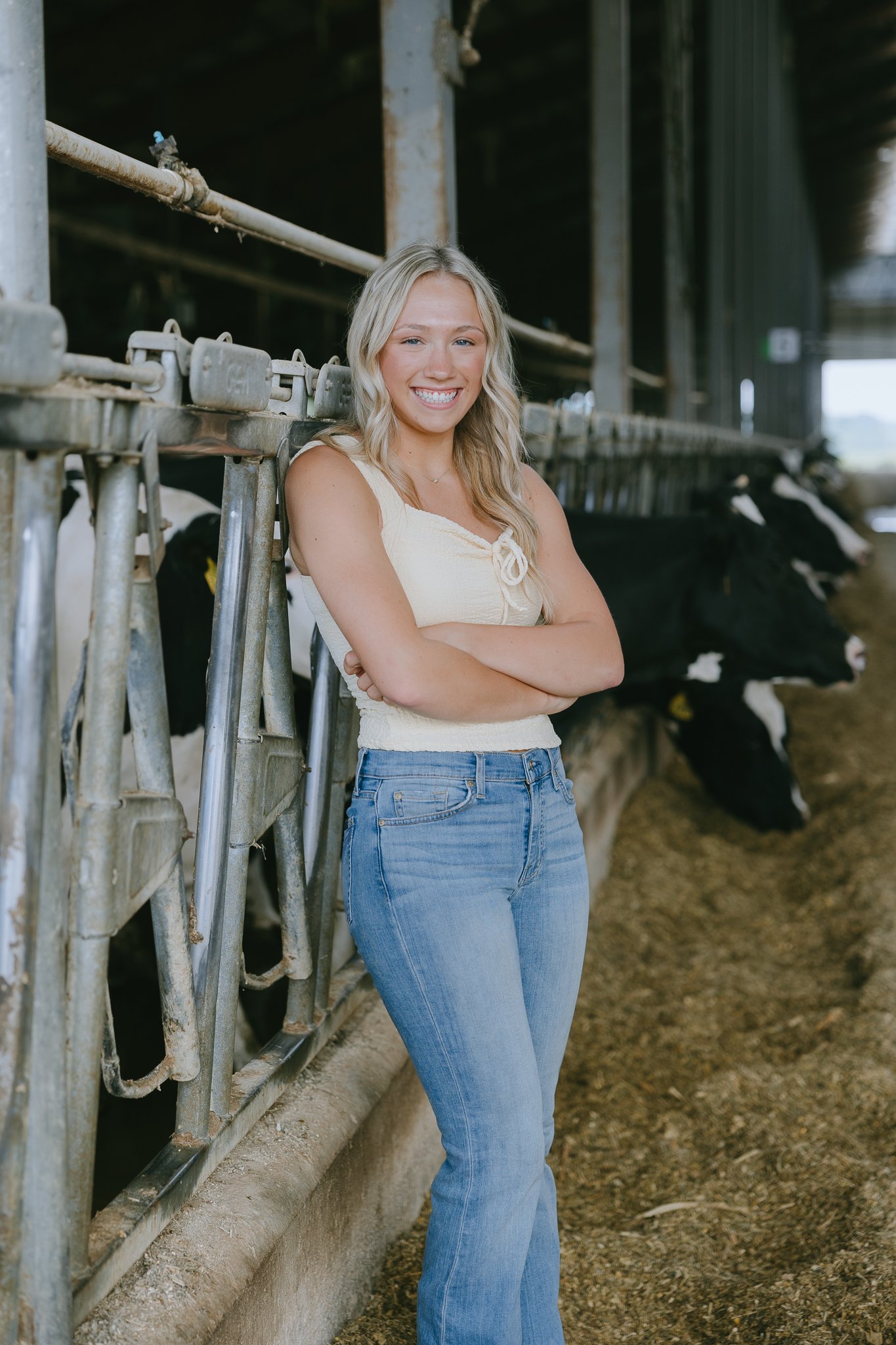 A young woman with blonde hair standing in a barn with black and white cows.