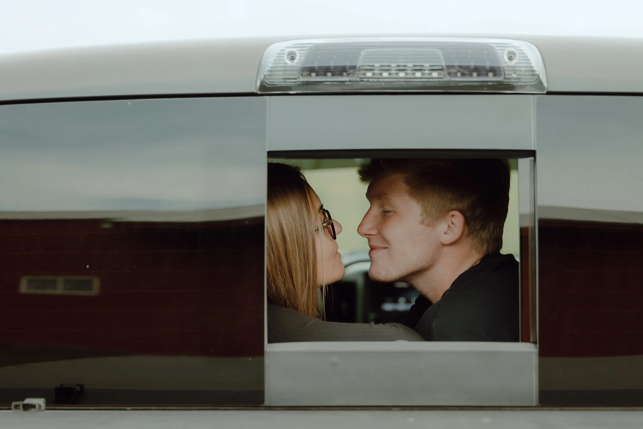 A couple sitting inside a bus, facing each other with their noses nearly touching, sharing a close moment.