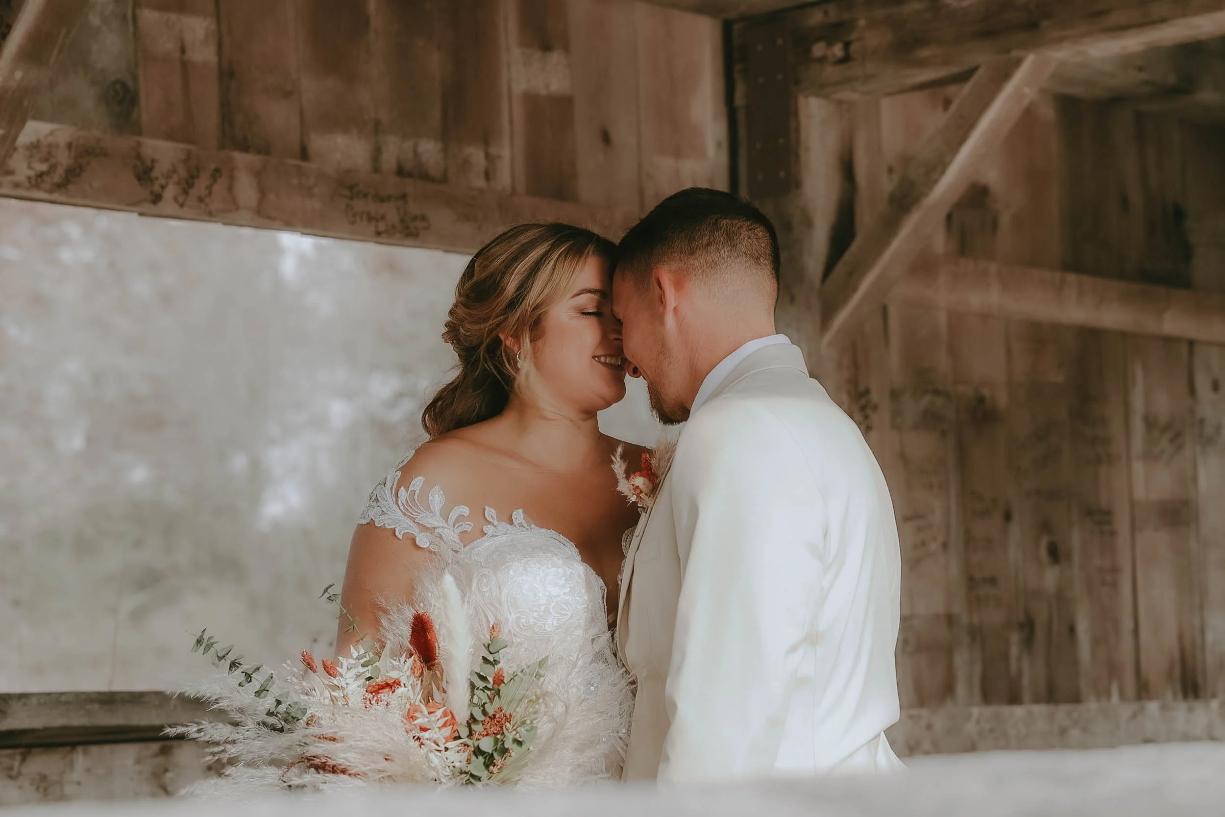 Bride and groom sharing a moment with foreheads touching, smiling, in a rustic wooden setting.