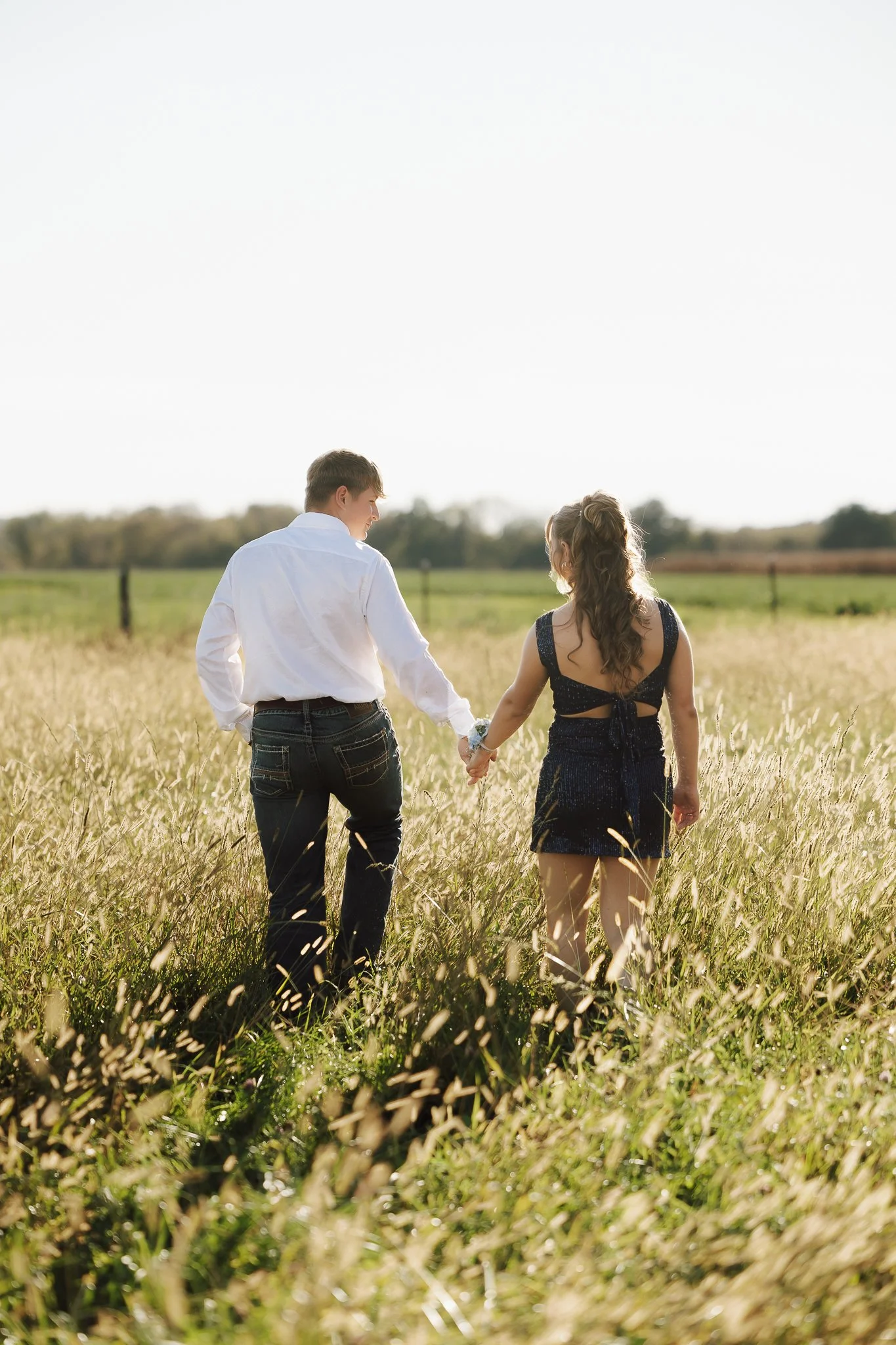A young couple holding hands and walking through a grassy field during daylight.