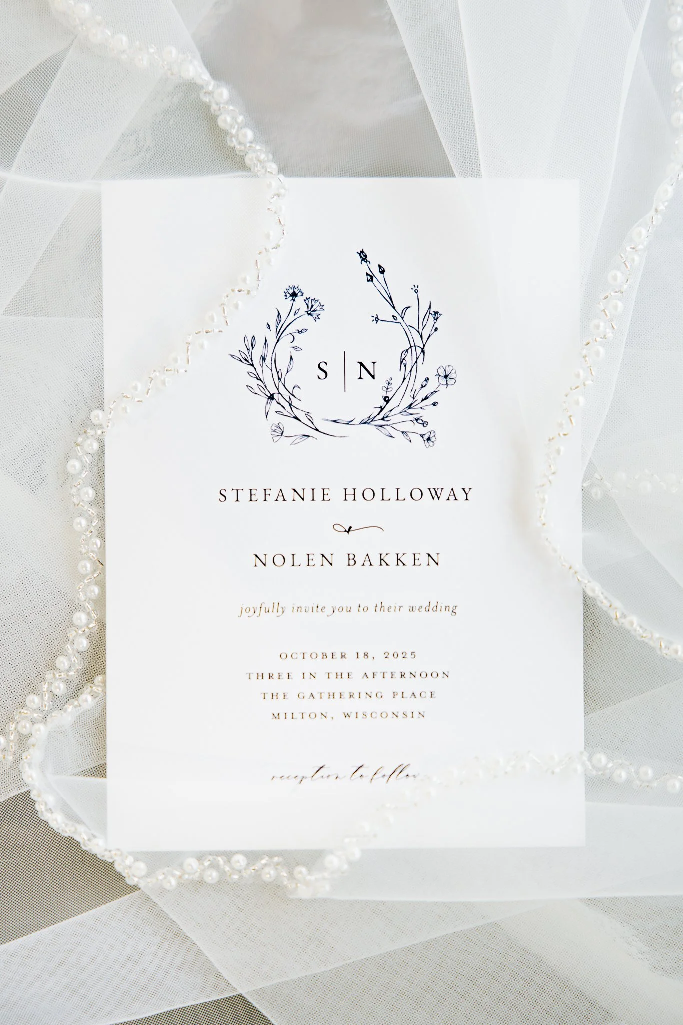 Wedding invitation with floral design and monogram, surrounded by pearl and tulle embellishments.