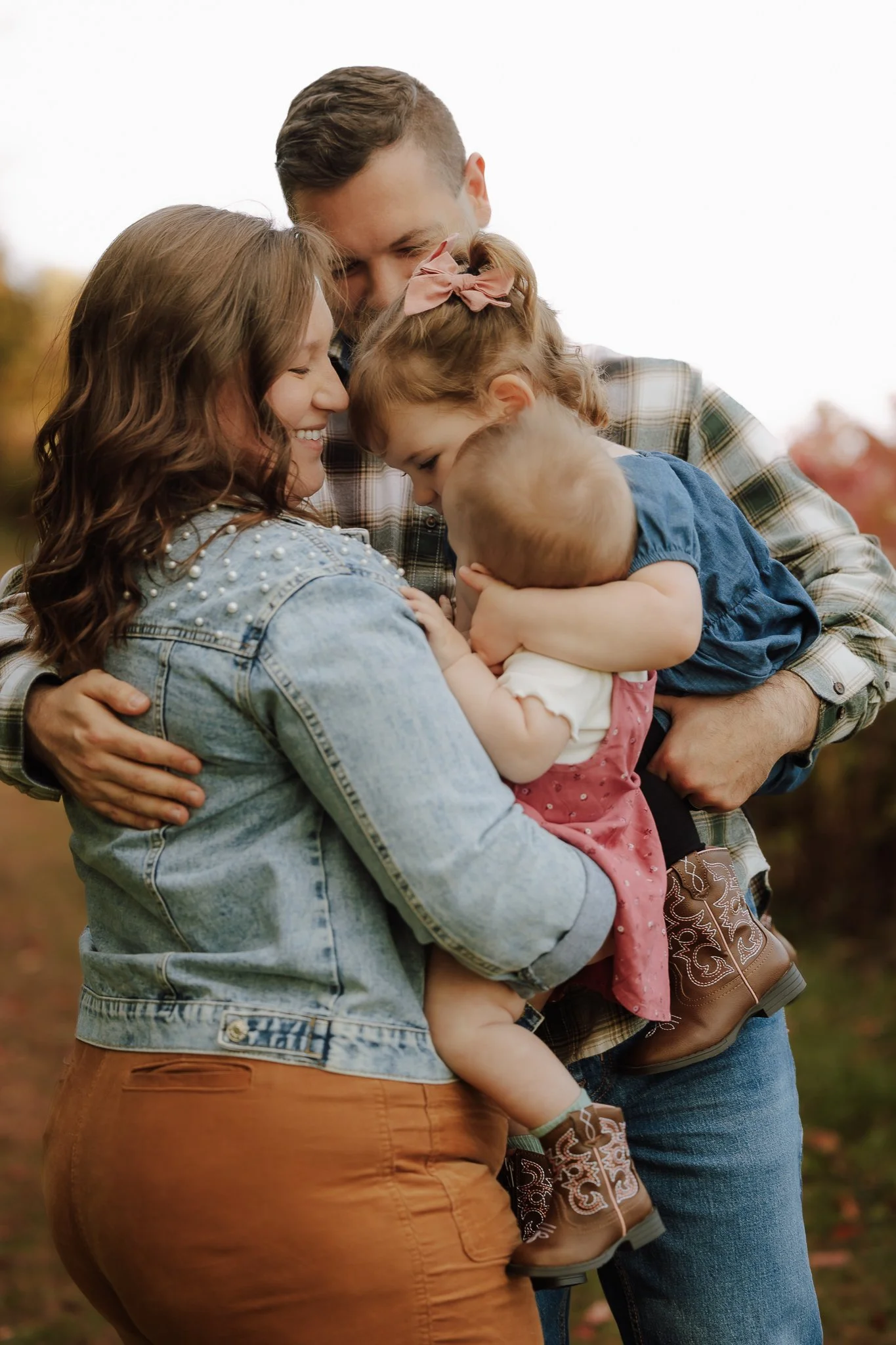 A family of four embracing outdoors during autumn, with fall foliage in the background.