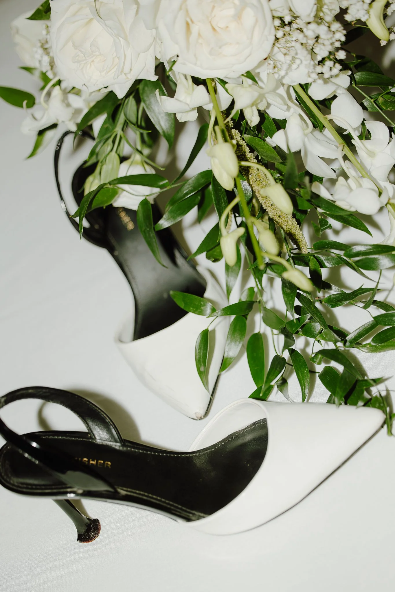A floral arrangement of white roses, calla lilies, and green foliage in black and white vases.