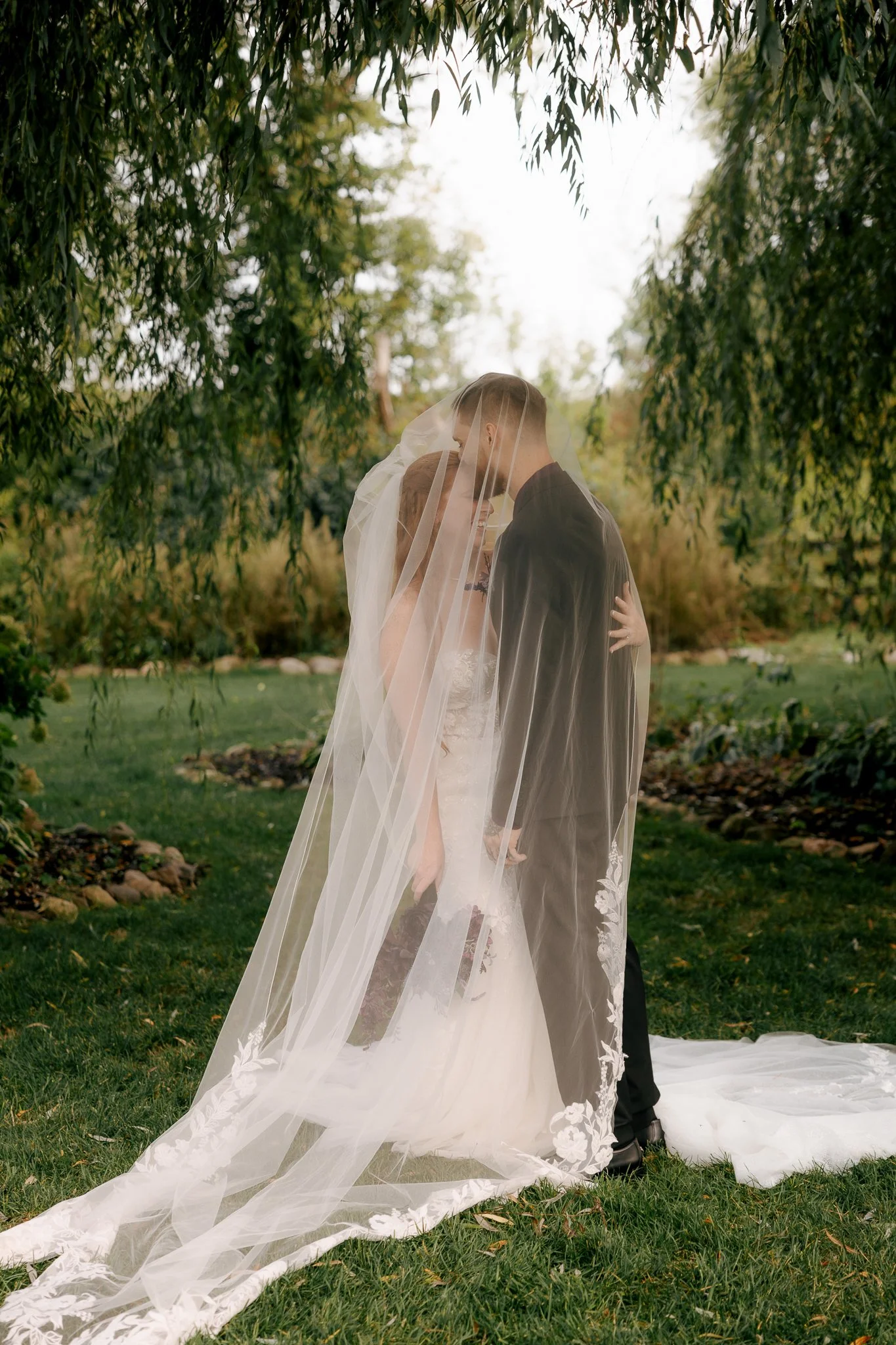 couple under veil while groom kisses bride on the forehead