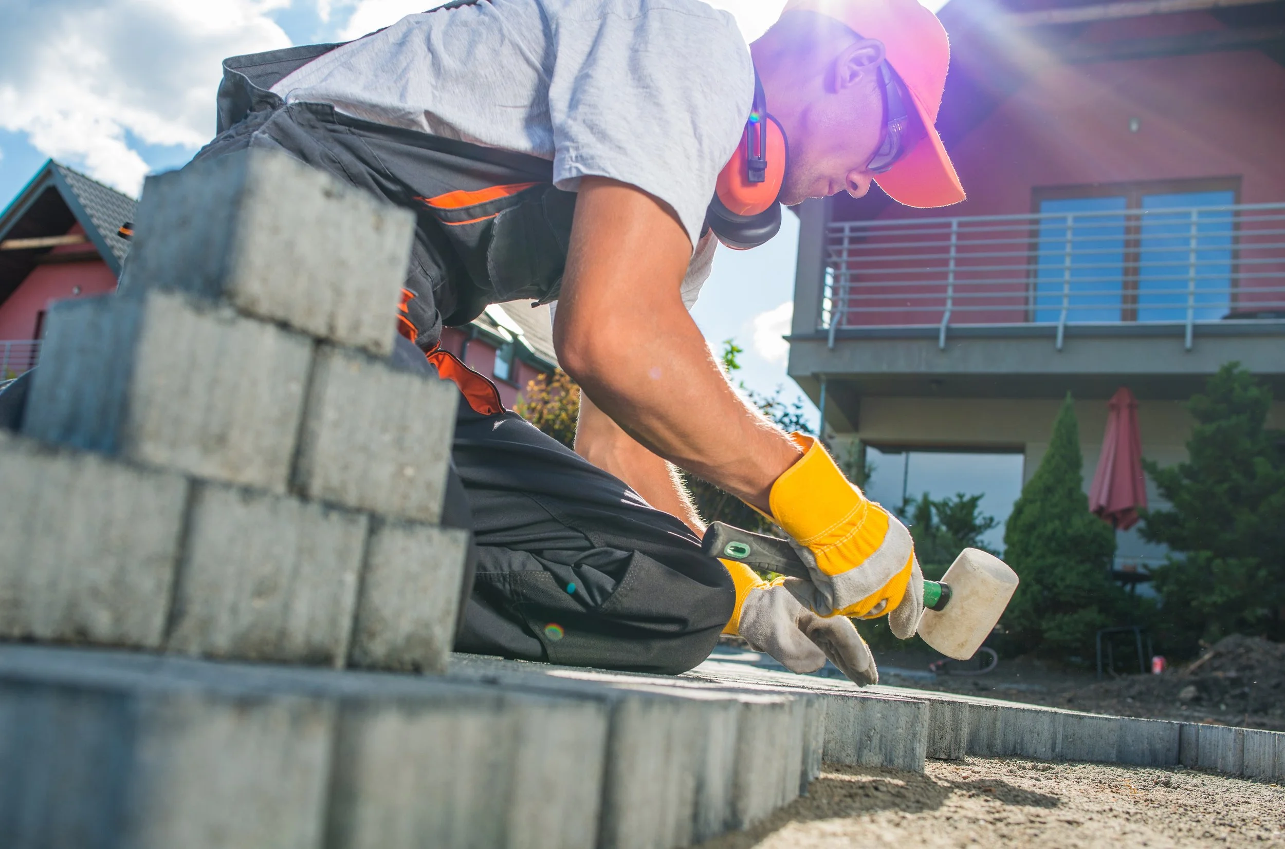 A construction worker in safety gear laying concrete blocks for a pavement.