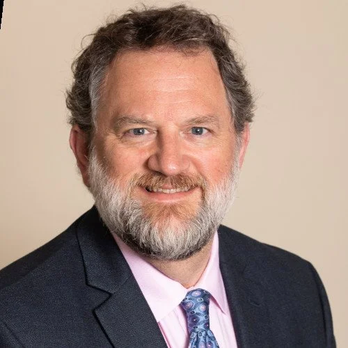 Man in suit with beard and smiling against beige background