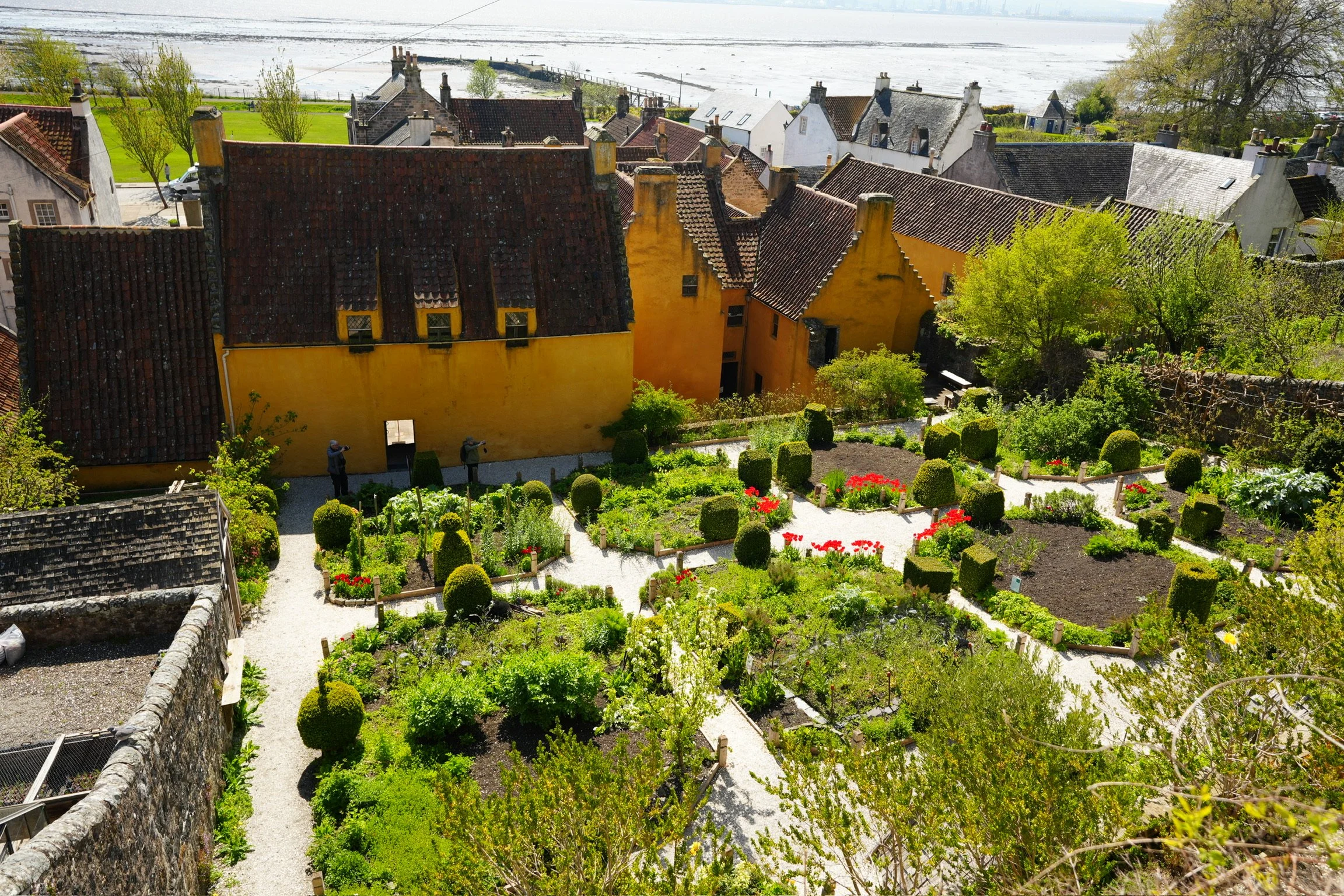 A scenic view of a quaint coastal town with colorful houses, a well-maintained garden, and a body of water in the background.