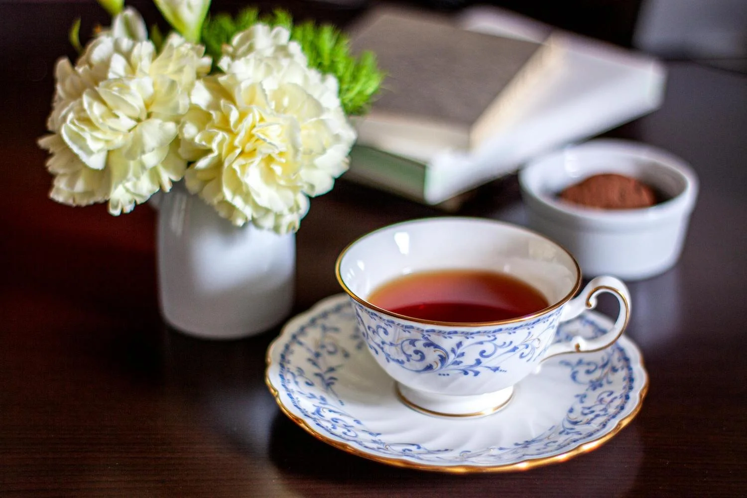 Cup of British tea on a saucer beside flowers and a book, representing a calm tea moment in England.