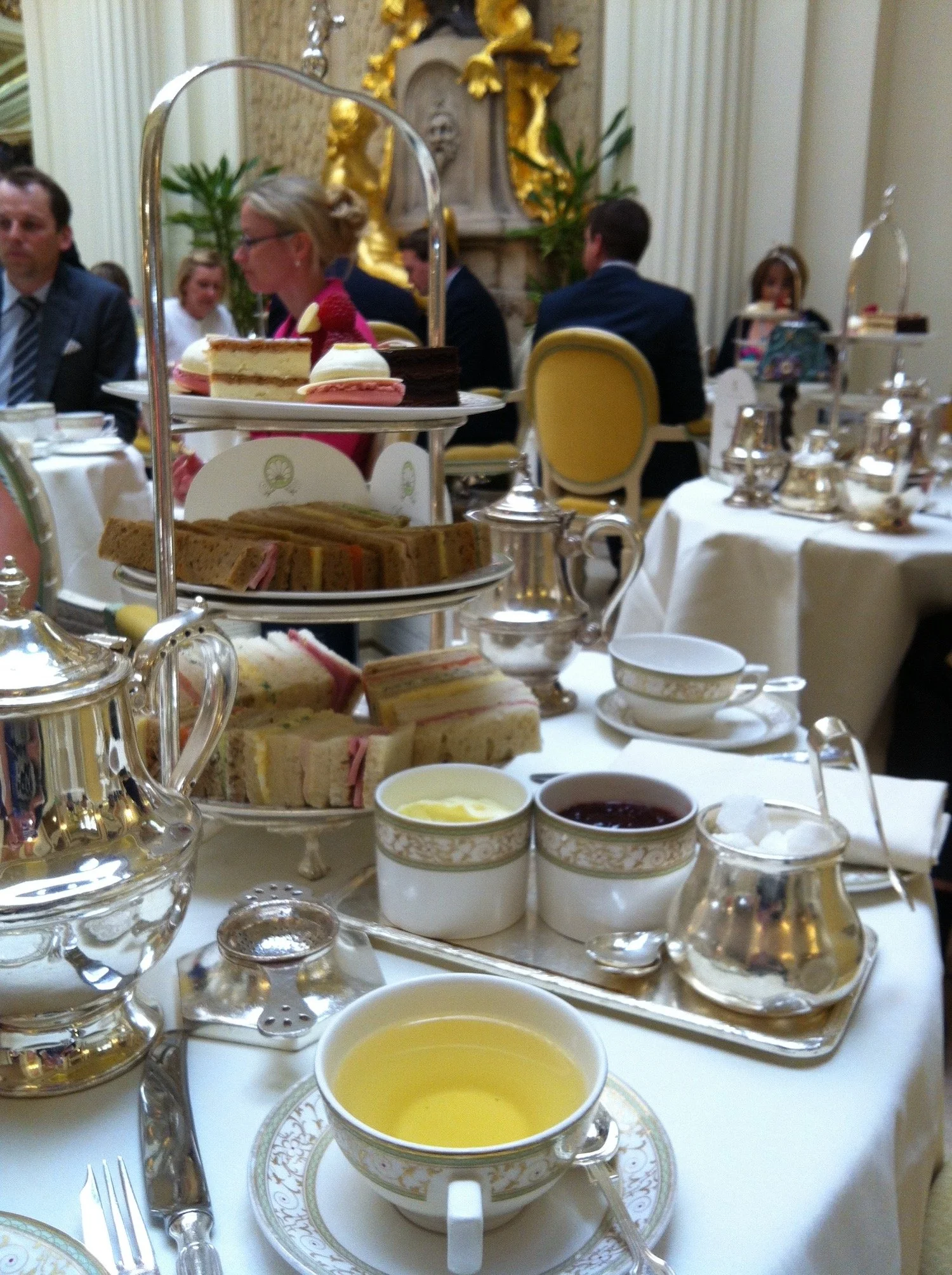 Traditional afternoon tea in England with a tiered stand of sandwiches and cakes, silver teapots, and teacups in an elegant tea room.