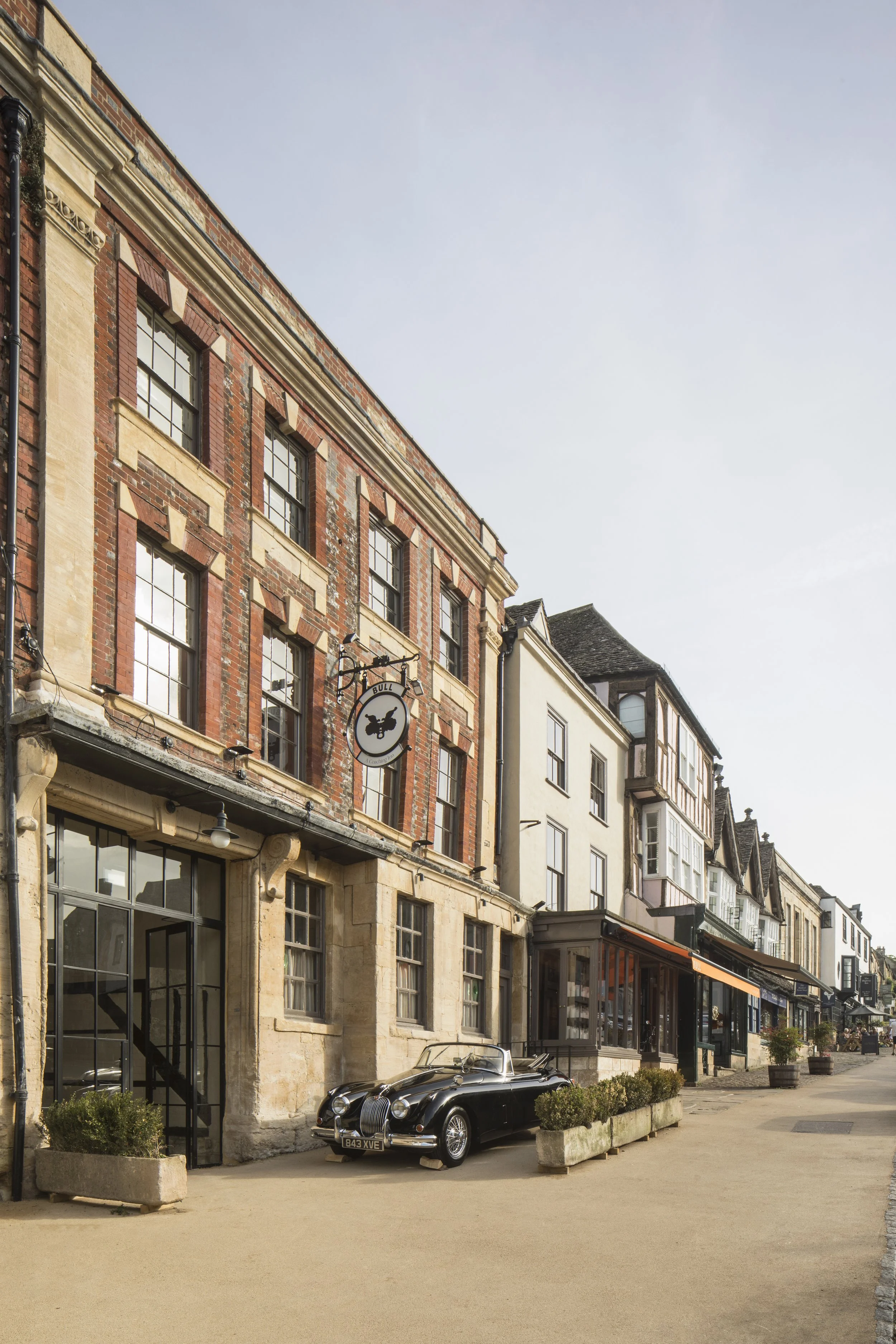 Historic brick buildings with shops and restaurants on a street, a vintage black car parked outside, and a clear sky above.