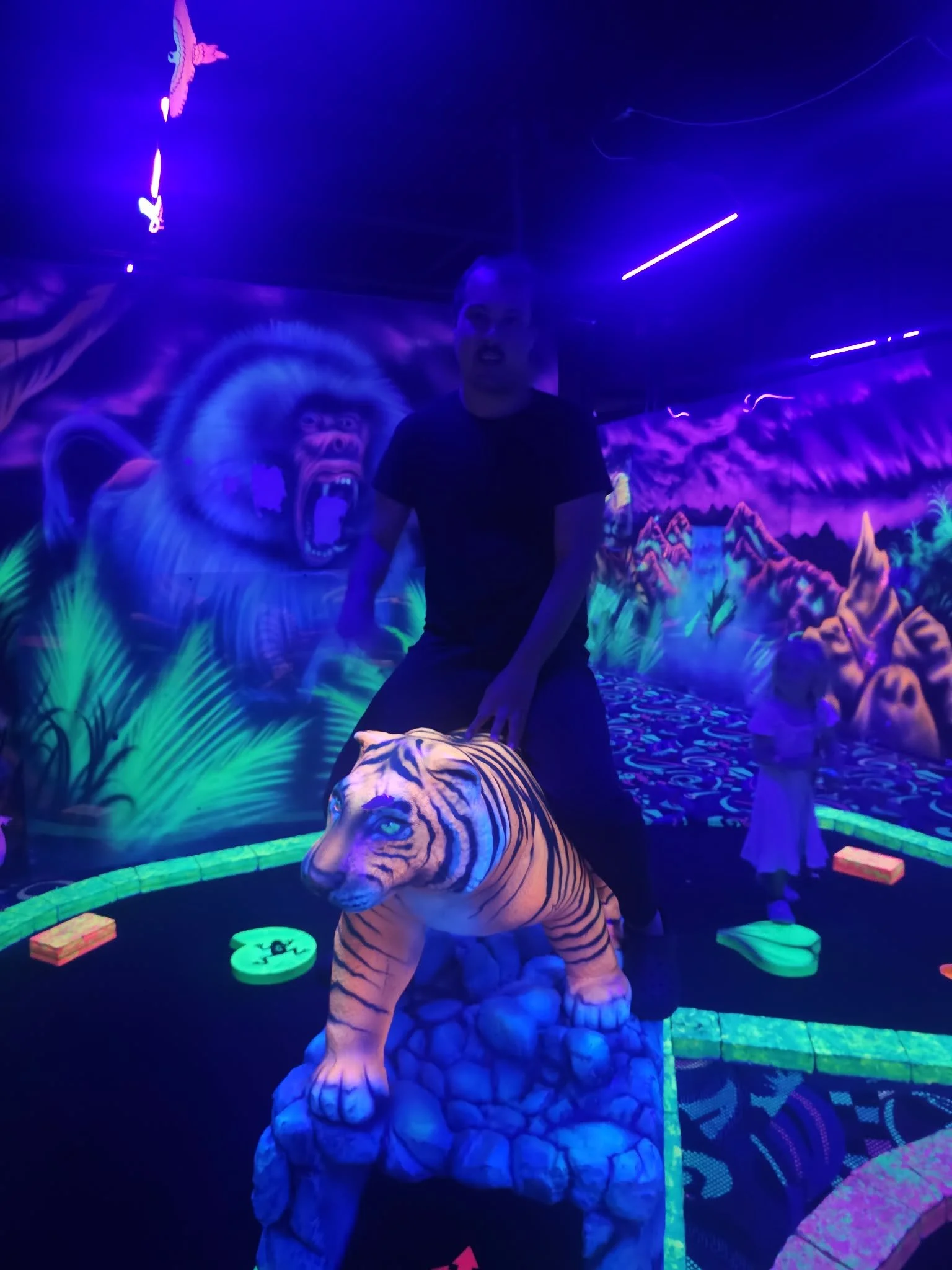 Person standing inside an LED glow-in-the-dark jungle scene with a painted tiger and a large monkey mural in the background.
