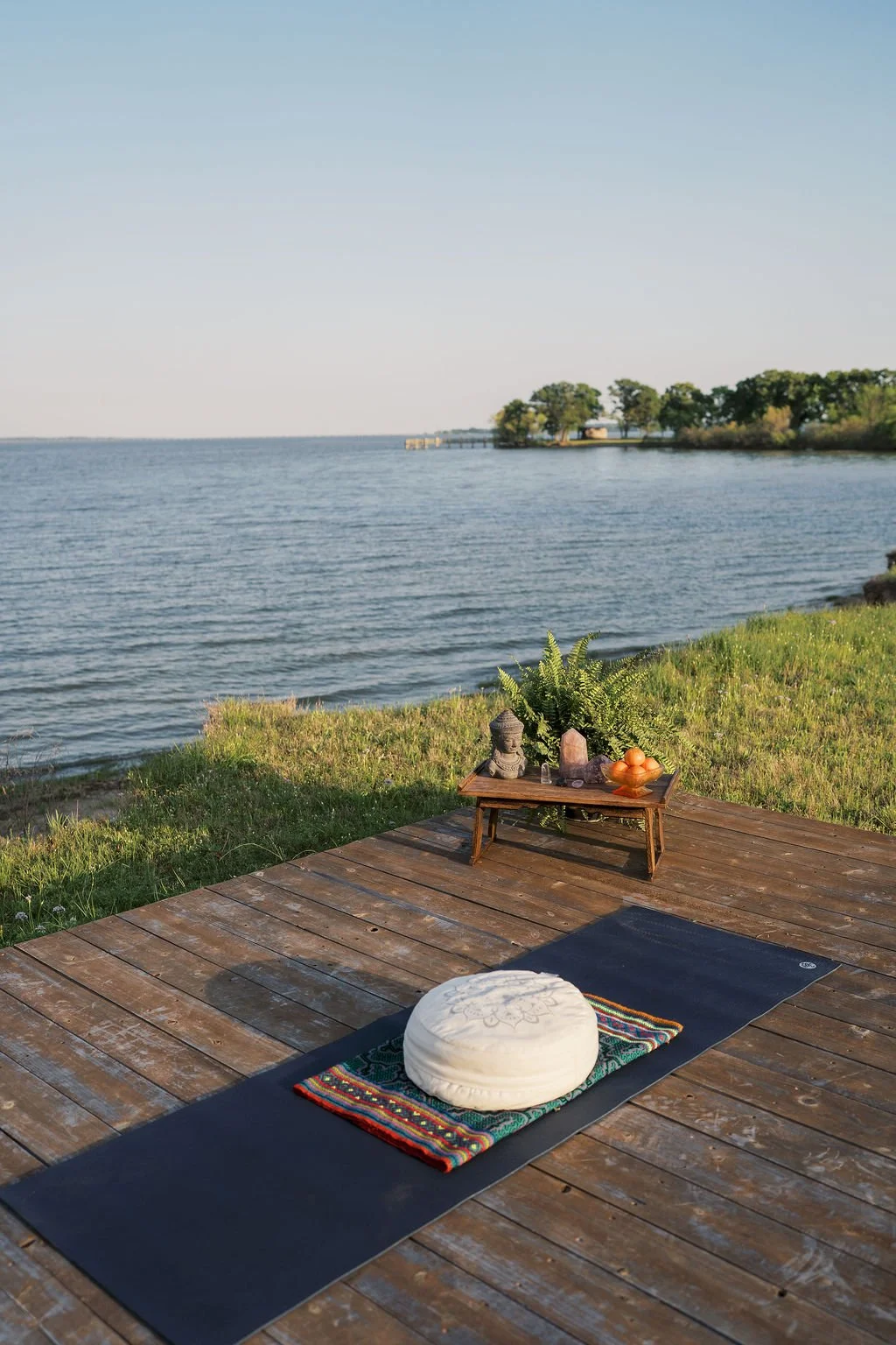 Yoga mat with cushion on a wooden deck overlooking lake tawakoni with trees in the background.