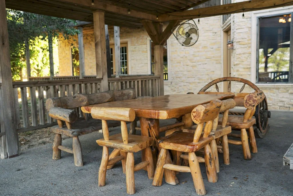 Rustic outdoor wooden dining set with a rectangular table and multiple logs as chairs, on a patio of our lodge at Peninsula Ranch in DFW  