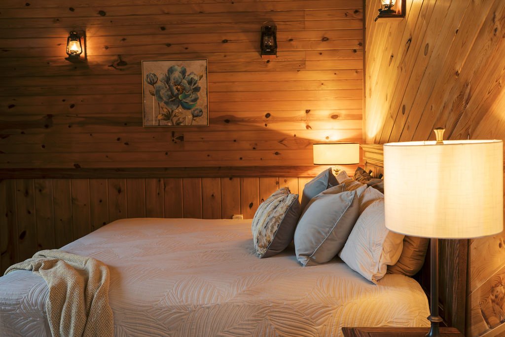 Cozy bedroom with wooden walls, a framed floral painting, and warm lighting from lamps and sconces at Peninsula Ranch in DFW 