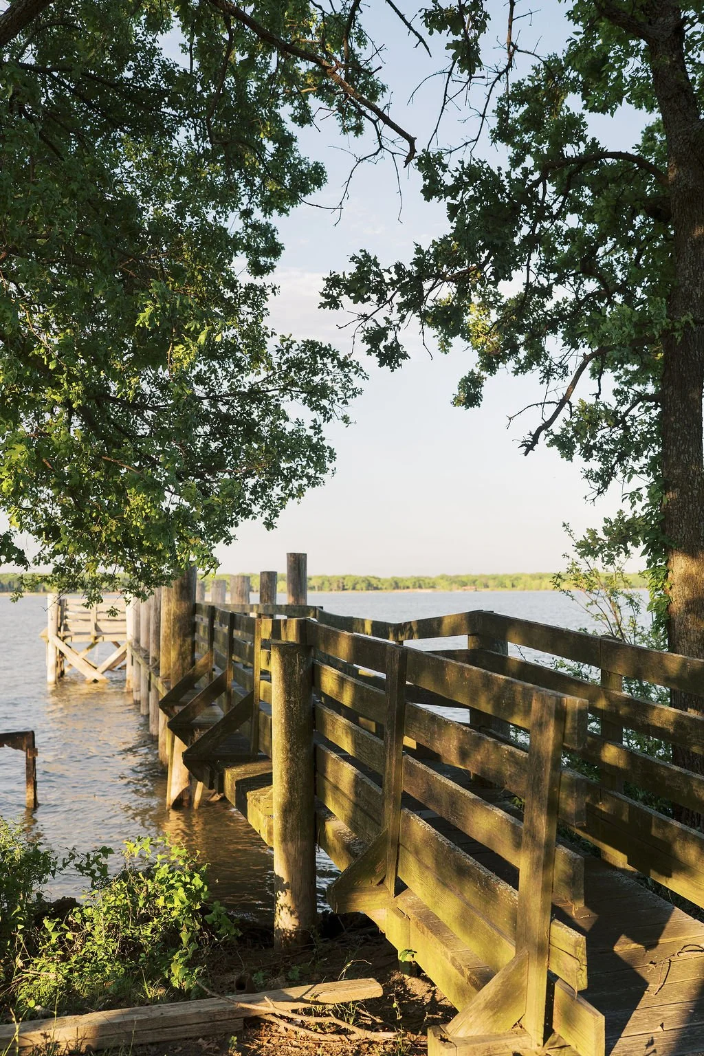 A wooden dock extends into Lake Tawakoni, framed by trees with green leaves, under a clear sky at Peninsula Ranch in DFW 