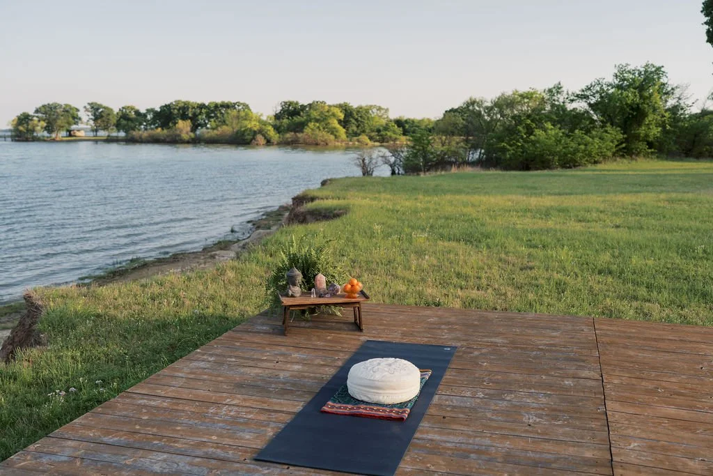 Empty yoga mat with a round white cushion on top, placed on a wooden deck outdoors by Lake Tawakoni, with a small wooden table at Peninsula Ranch in DFW 