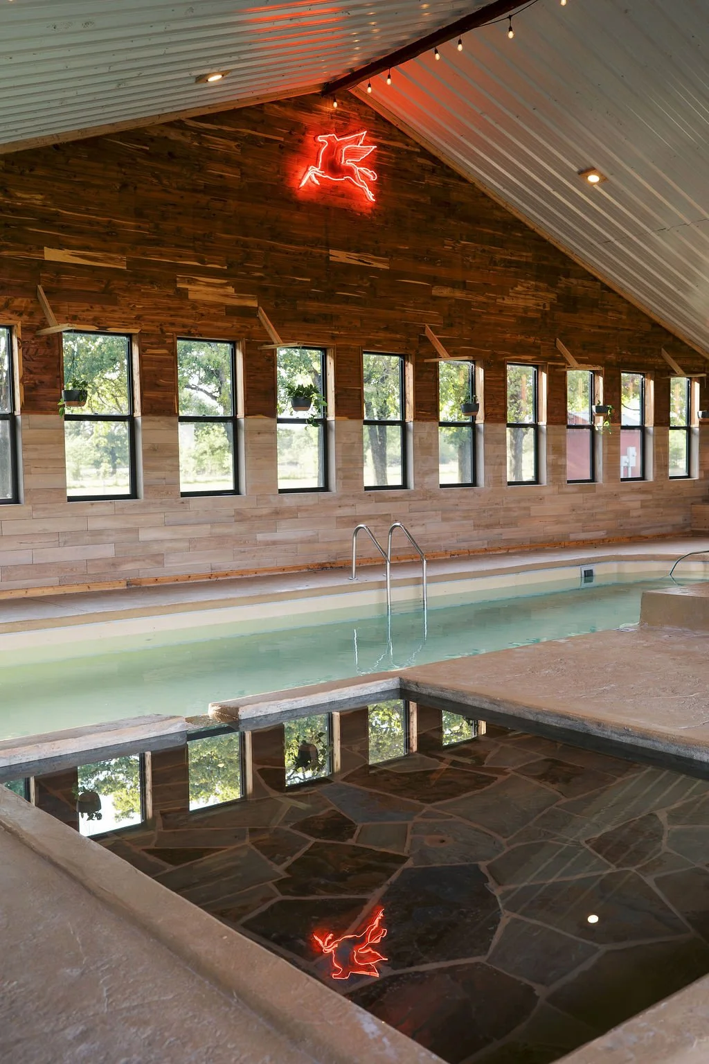 Indoor swimming pool at Peninsula Ranch in quinlan, Texas with wooden walls, multiple windows, and a neon unicorn sign on the wall.