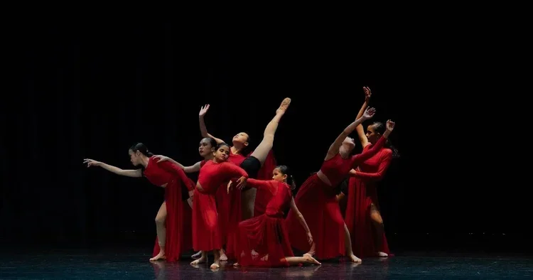 Group of female dancers in red costumes performing on stage with black background