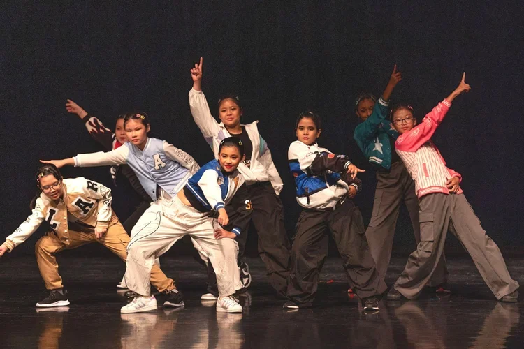Eight young girls in colorful casual clothing striking dance poses on a stage.