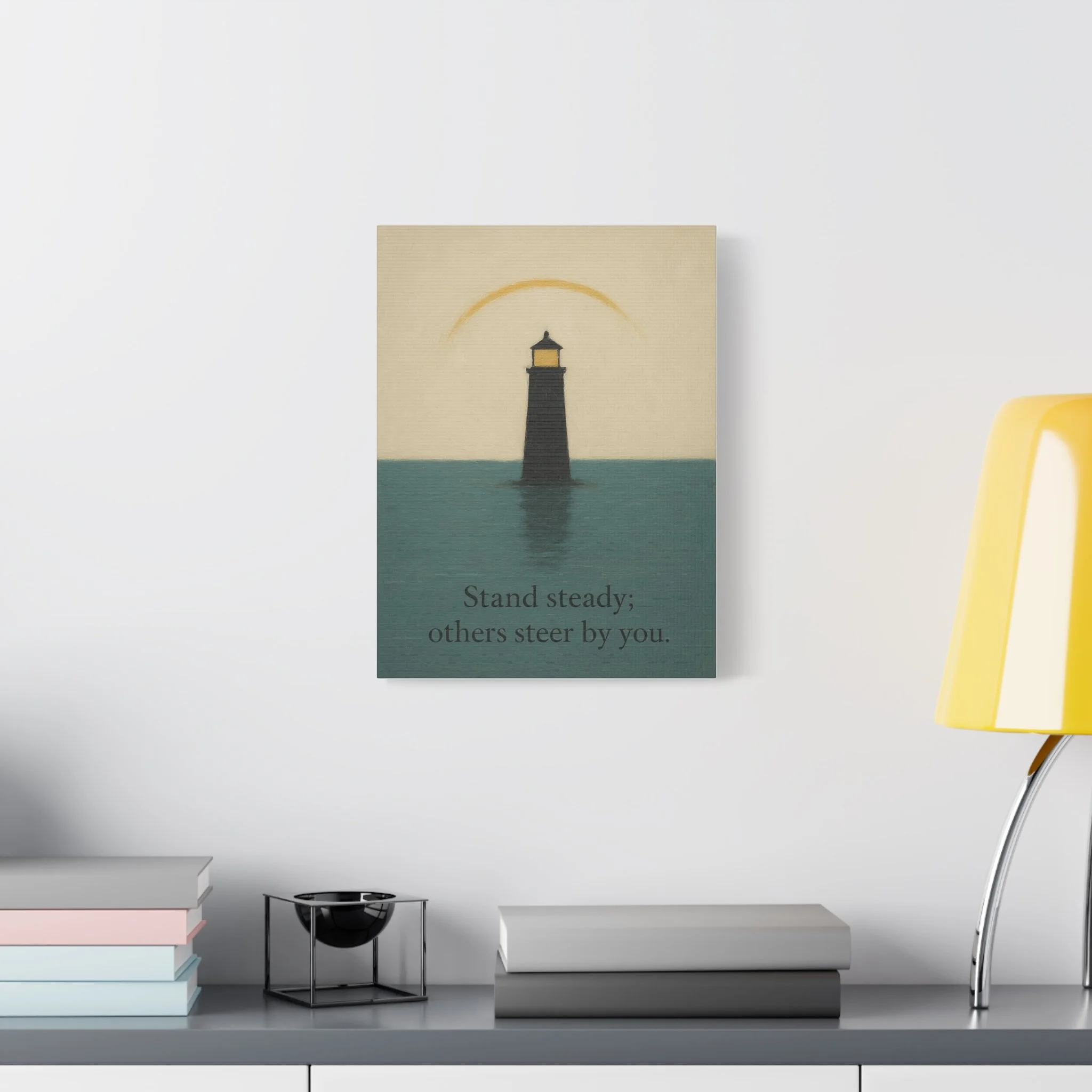 Room mockup of lighthouse canvas on a light wall above a tabletop with books and a yellow lamp.