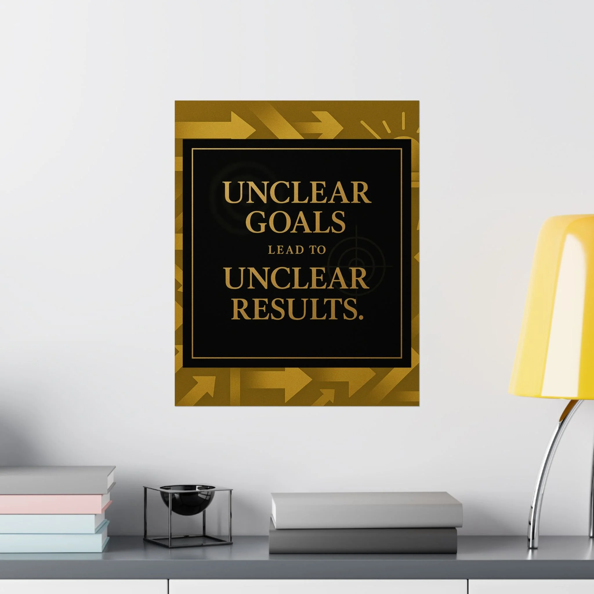 Room mockup of black-and-gold “Unclear Goals Lead to Unclear Results” poster above a tabletop with books and a yellow lamp.