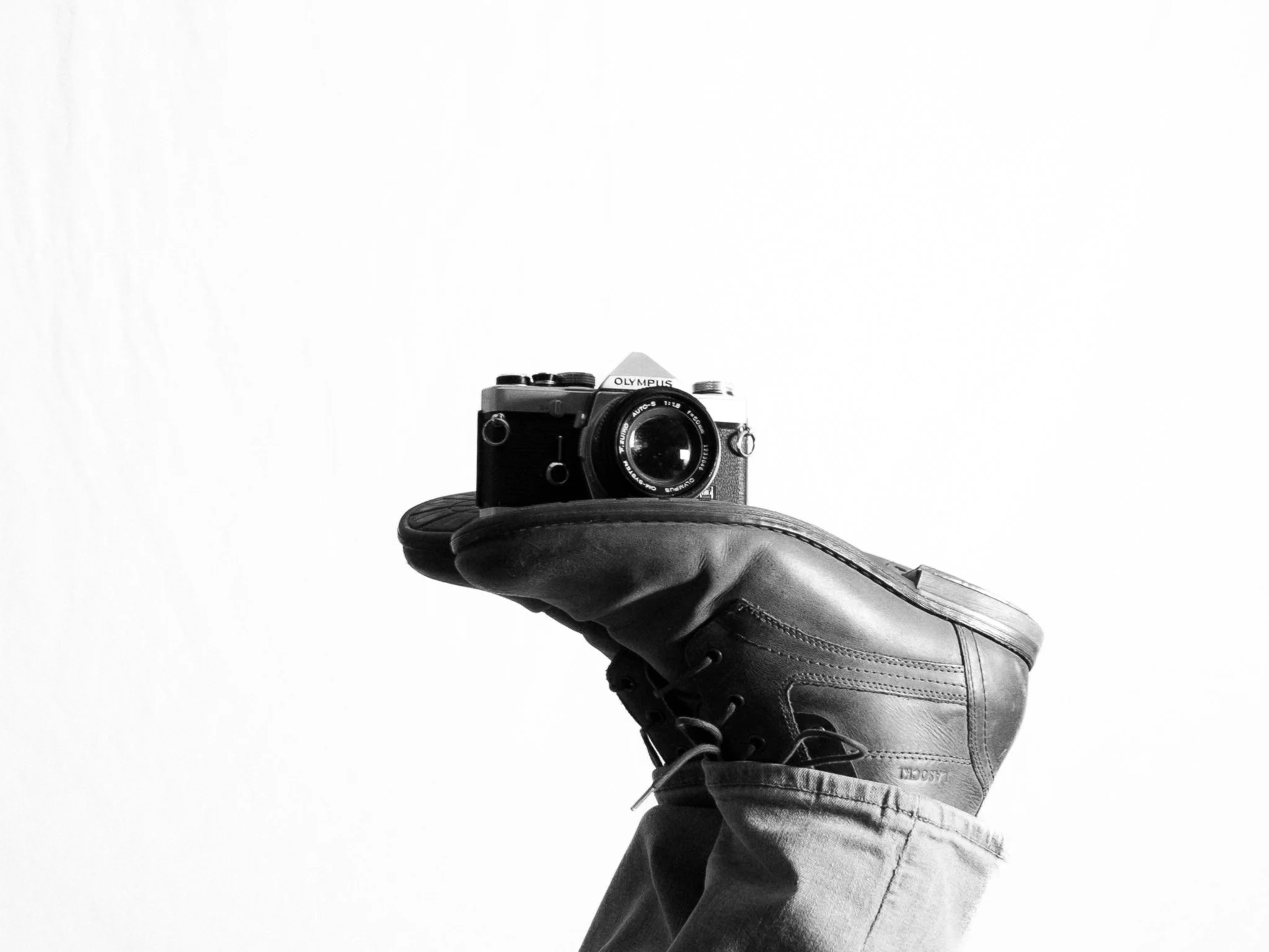 Person in a boot and jeans holding a camera against a plain background.