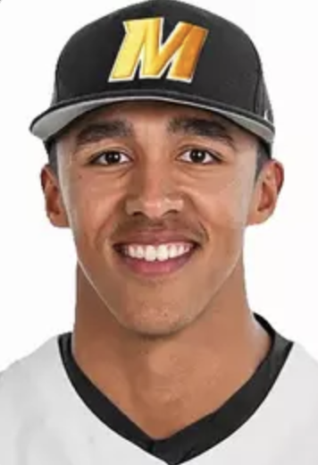Close-up of a young man wearing a baseball cap with a yellow 'M' logo and a white jersey with black trim, smiling at the camera.