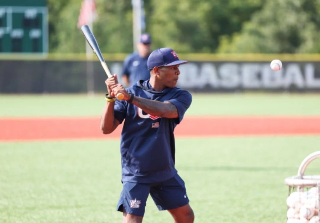 A young male baseball player in a blue uniform, wearing a cap, batting during practice on the field.