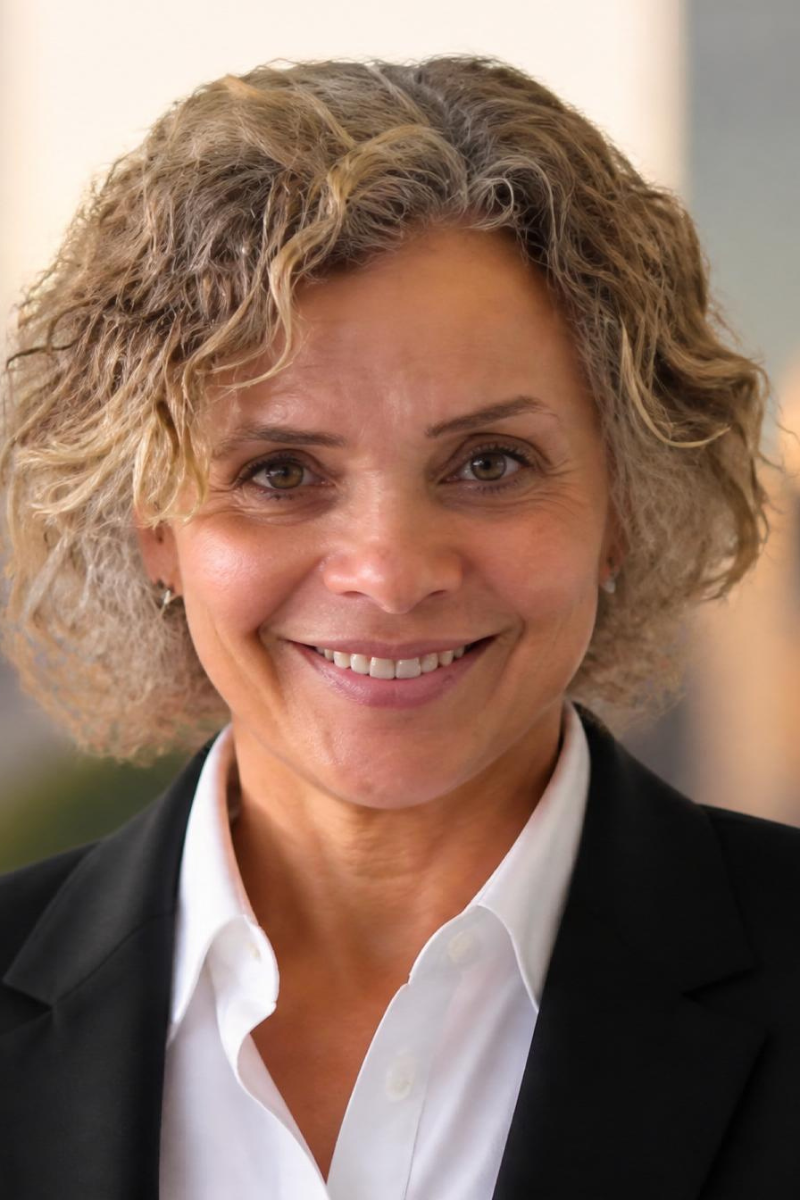 A woman with curly blonde hair smiling at the camera, wearing a black blazer and white shirt.